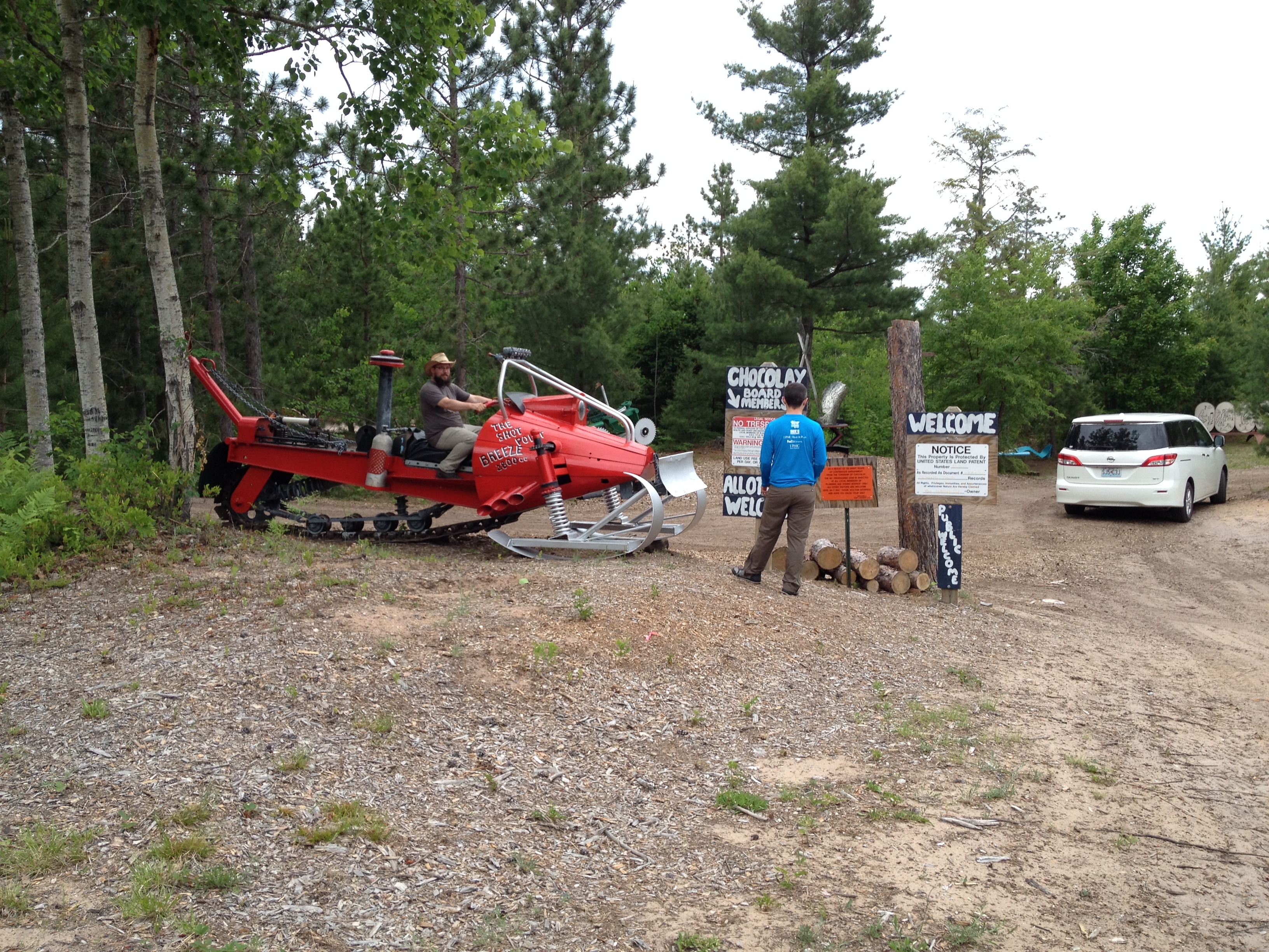 Gravel parking area at a wooded park entrance with a red tracked vehicle and signs.
