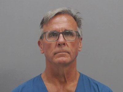 Man with gray hair and rectangular glasses photographed against a gray background.