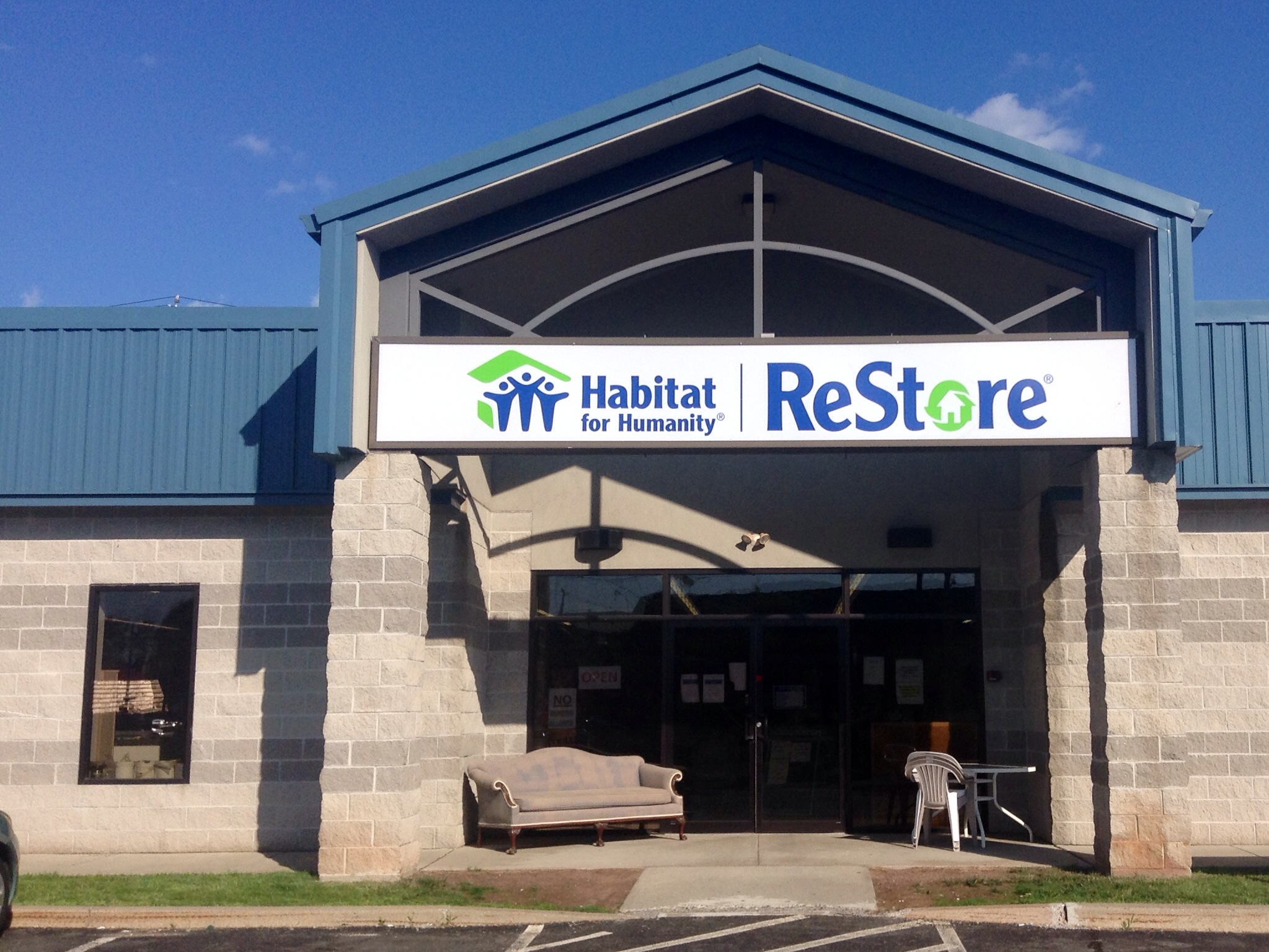 Exterior of a Habitat for Humanity ReStore with a sofa and chair outside the entrance.