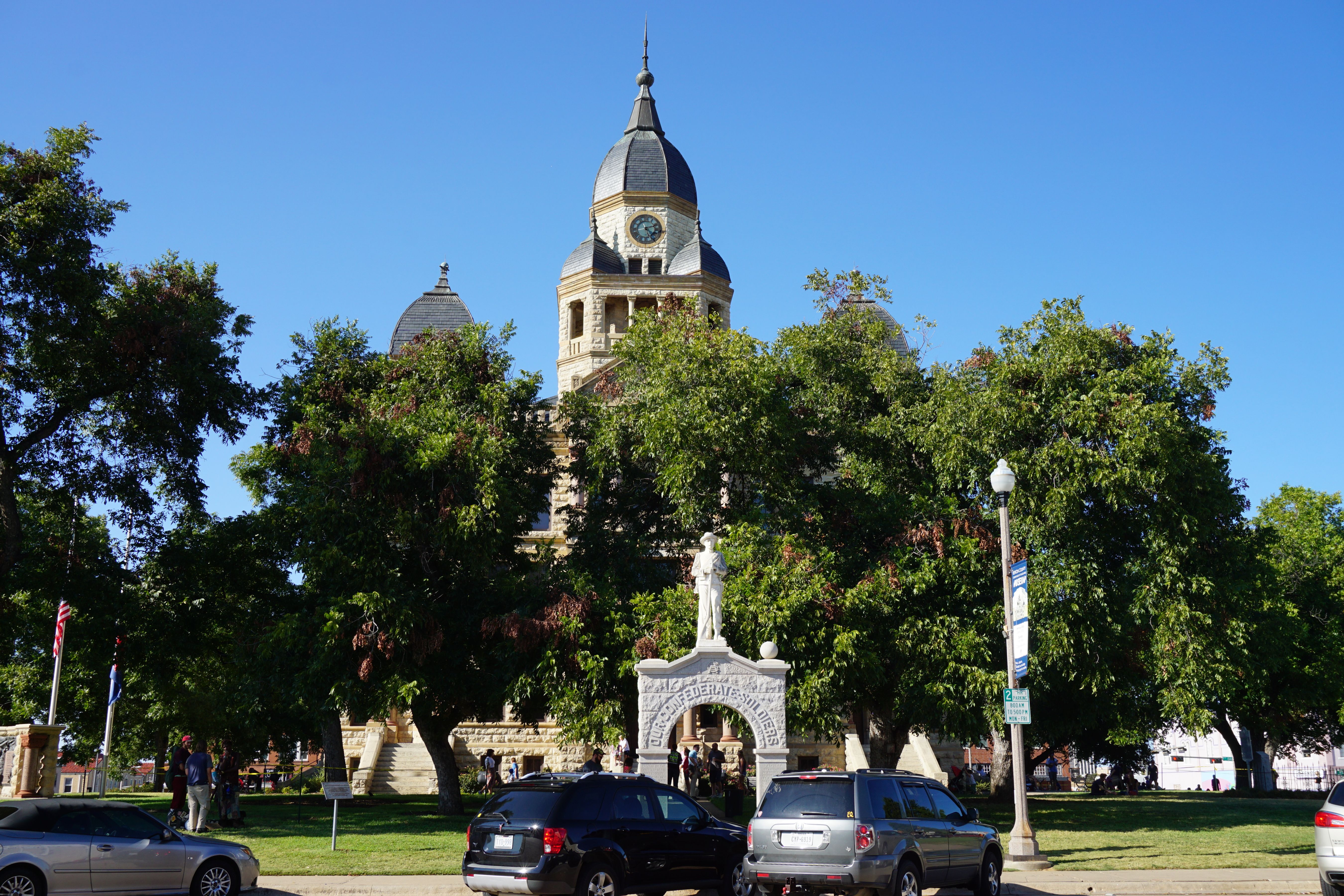 Historic stone courthouse with a domed clock tower and surrounding trees on a clear day.
