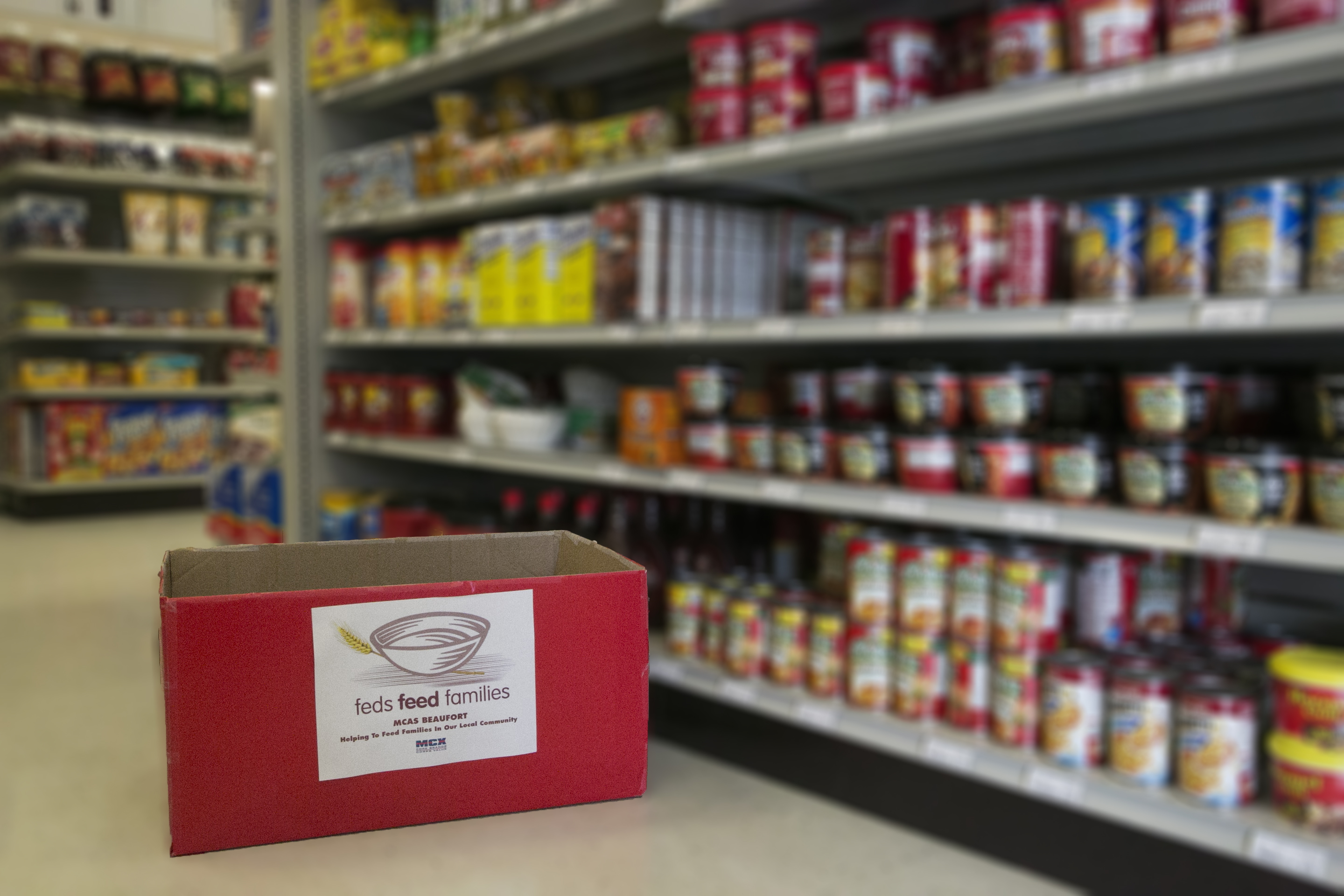 A red donation box in a grocery store aisle lined with canned goods.