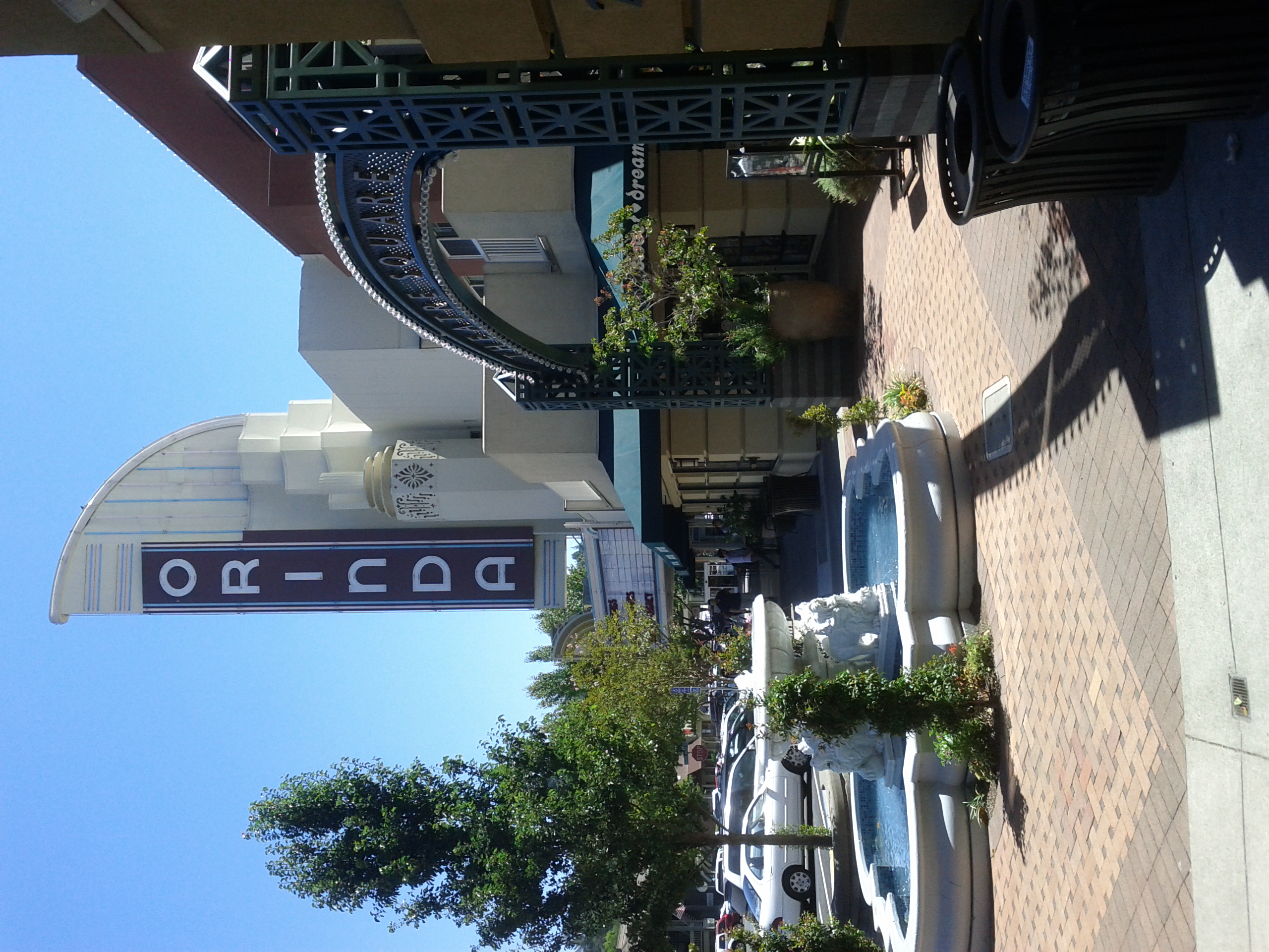 Art Deco theater exterior with a tall vertical sign, decorative fountain, and ornate iron archway.