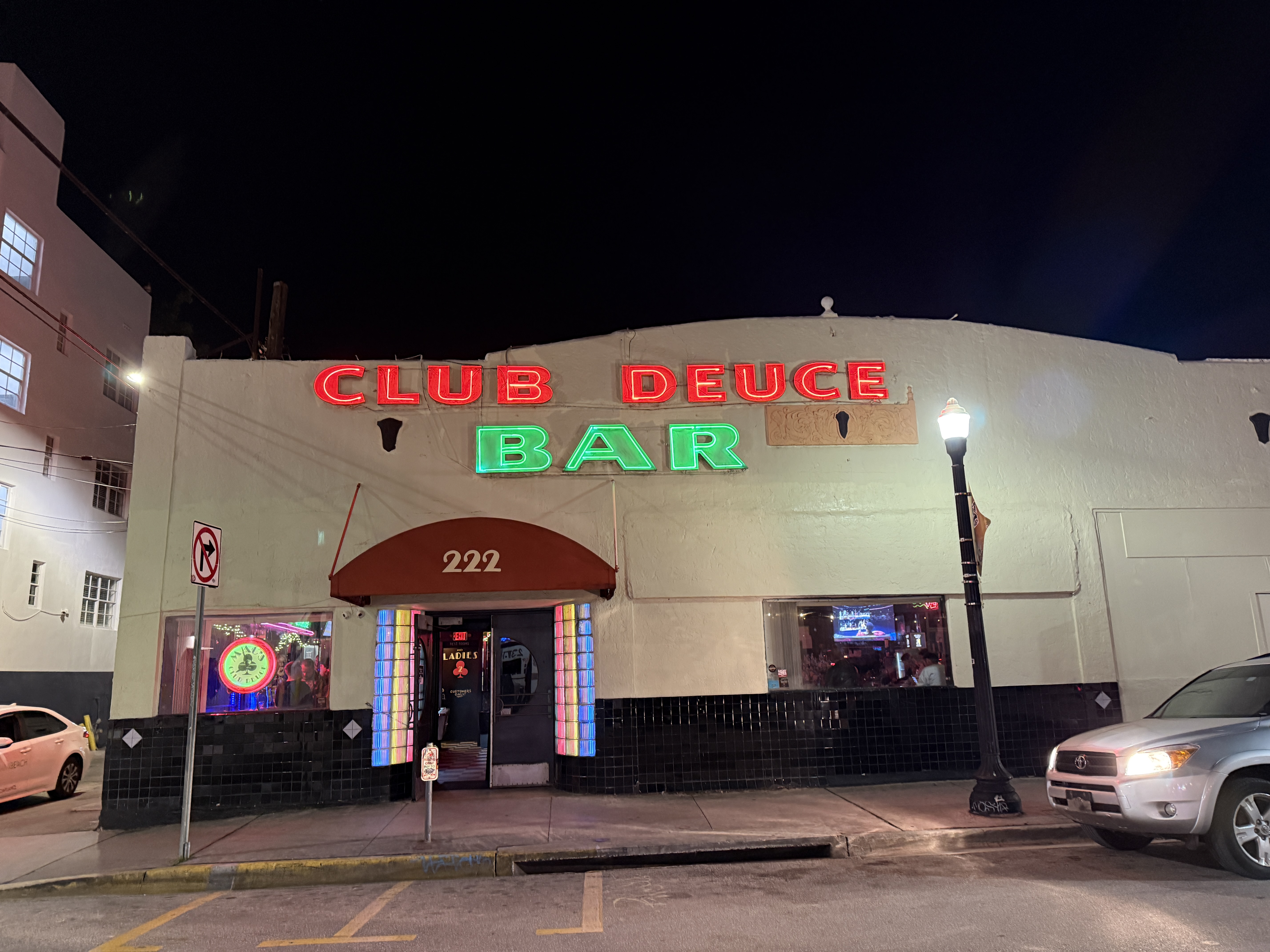 Bar exterior at night with neon red and green signs reading Club Deuce Bar.