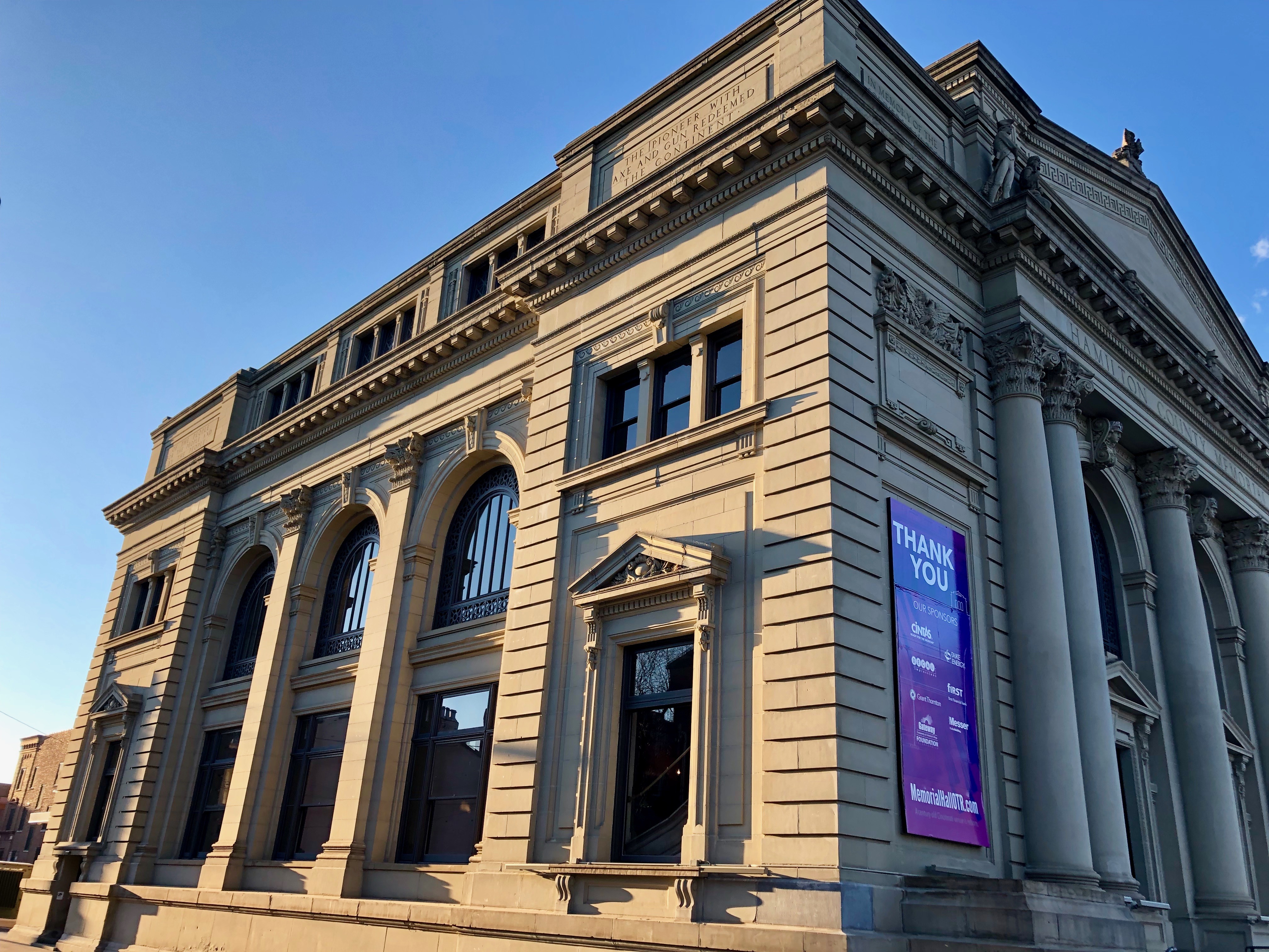 Neoclassical building facade with tall columns, arched windows, and a purple banner.