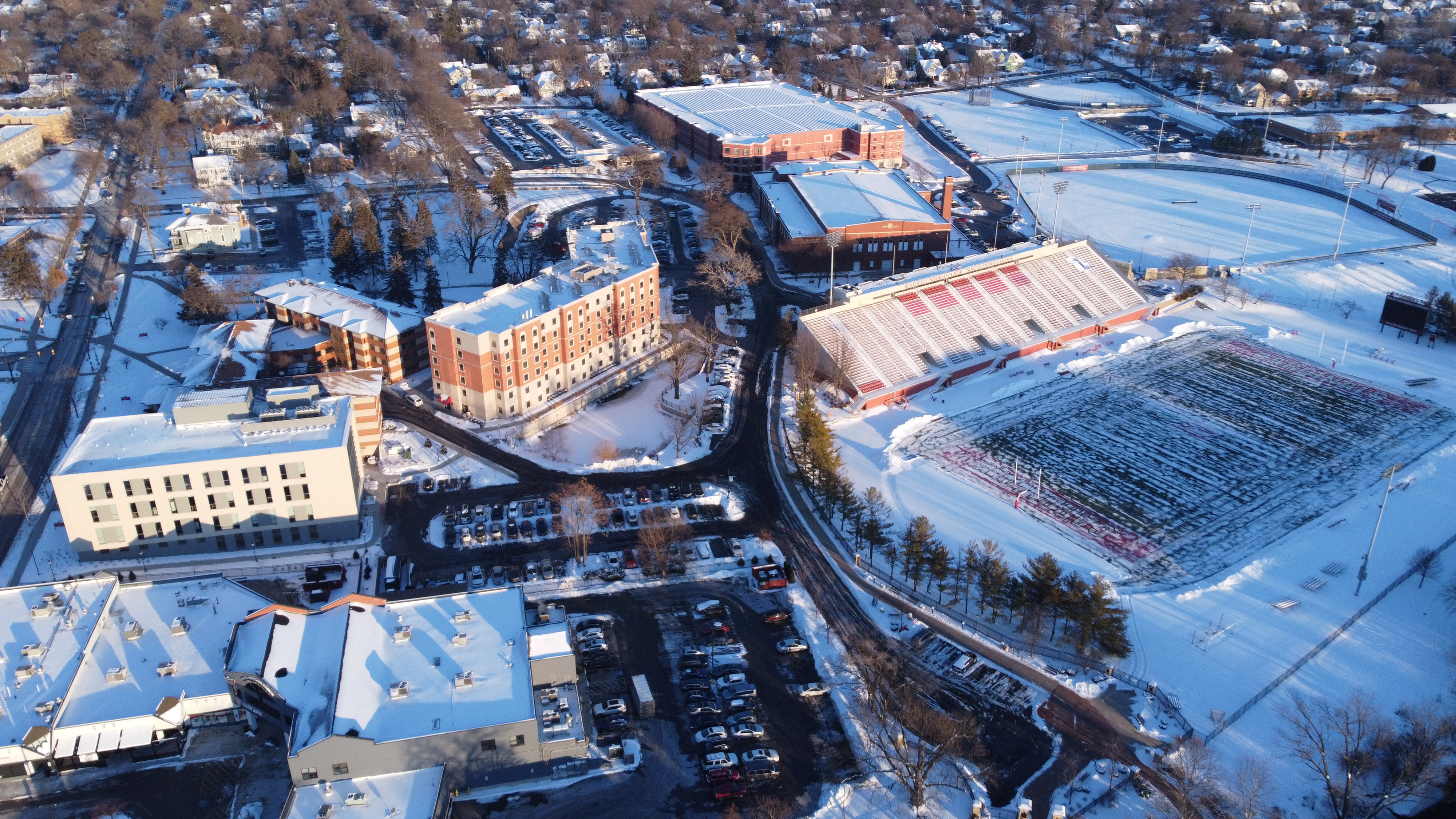 Aerial winter view of a college campus with brick buildings and a red-track stadium.