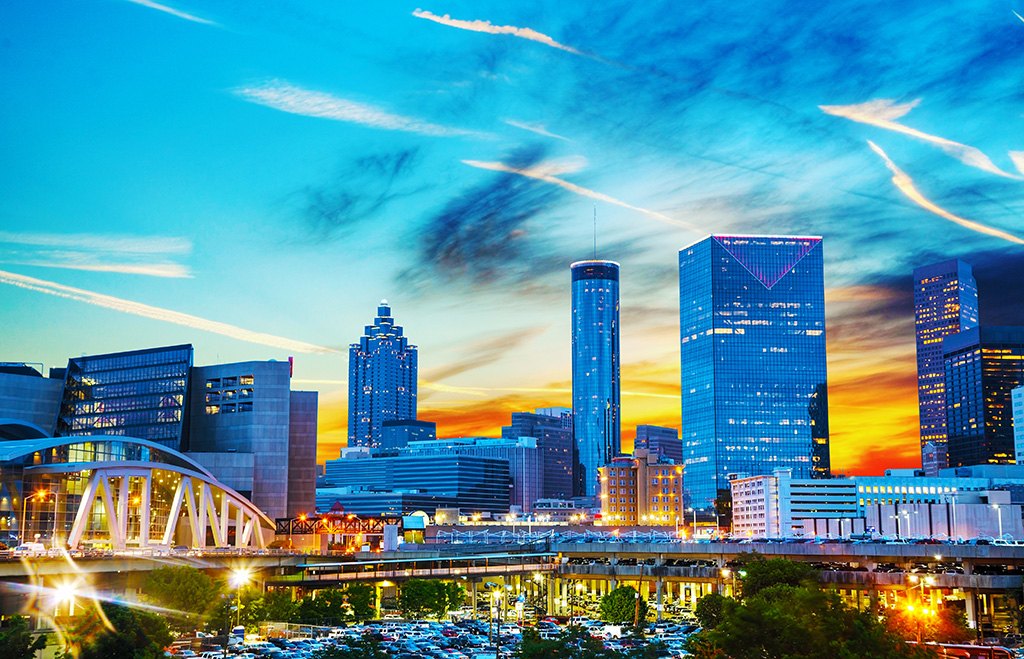 Downtown Atlanta skyline at sunset with illuminated skyscrapers and a highway bridge.