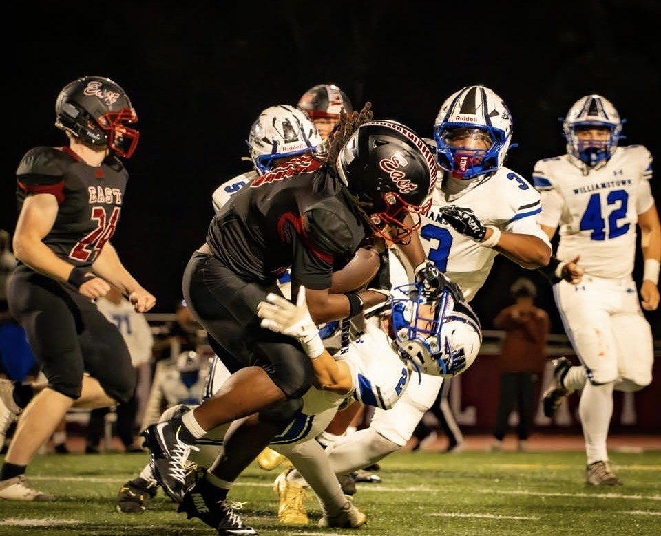 Football players in dark red uniforms tackle opponents in white and blue jerseys under stadium lights.