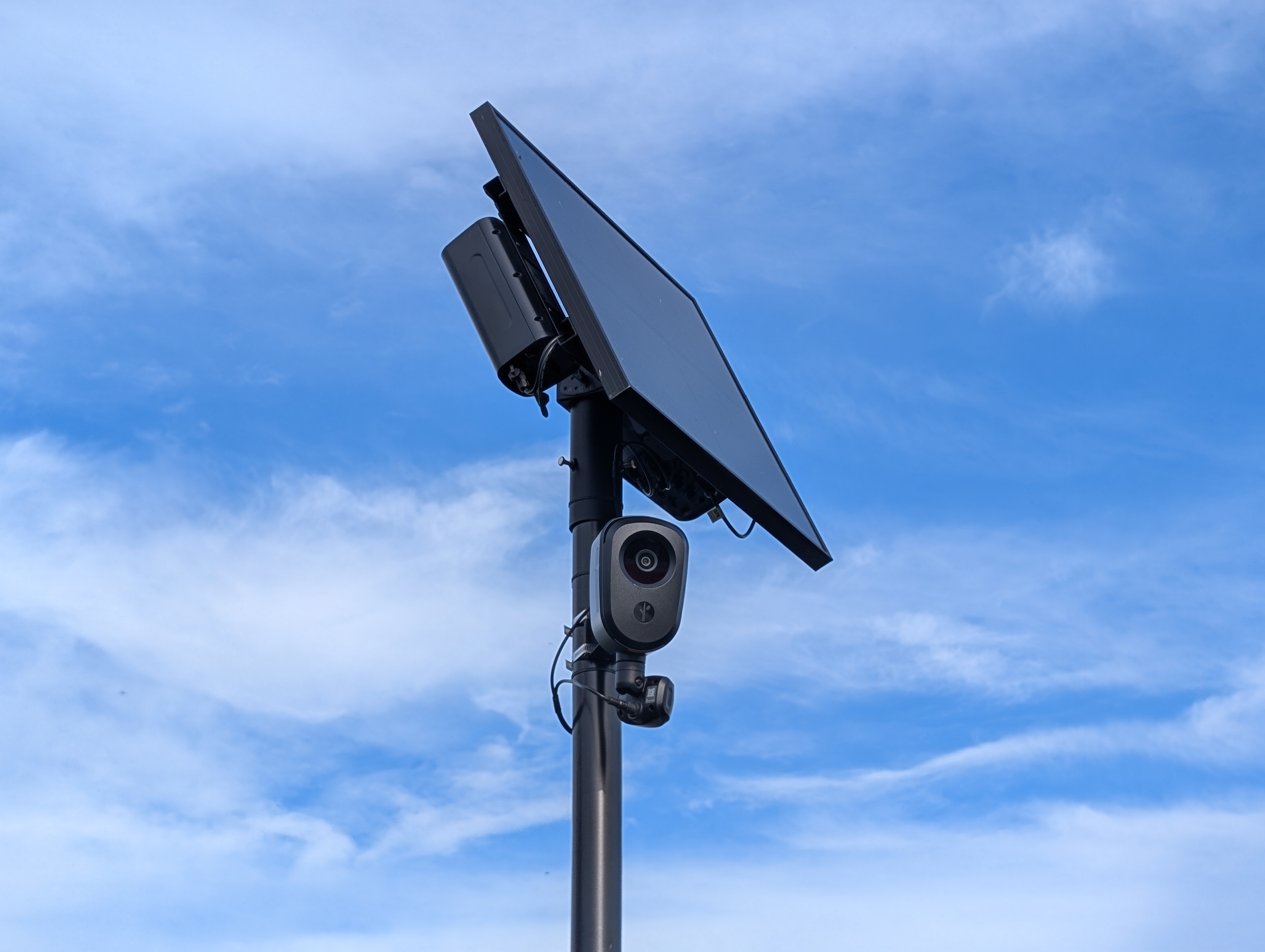Solar-powered license plate reader camera mounted on a metal pole against a cloudy sky.