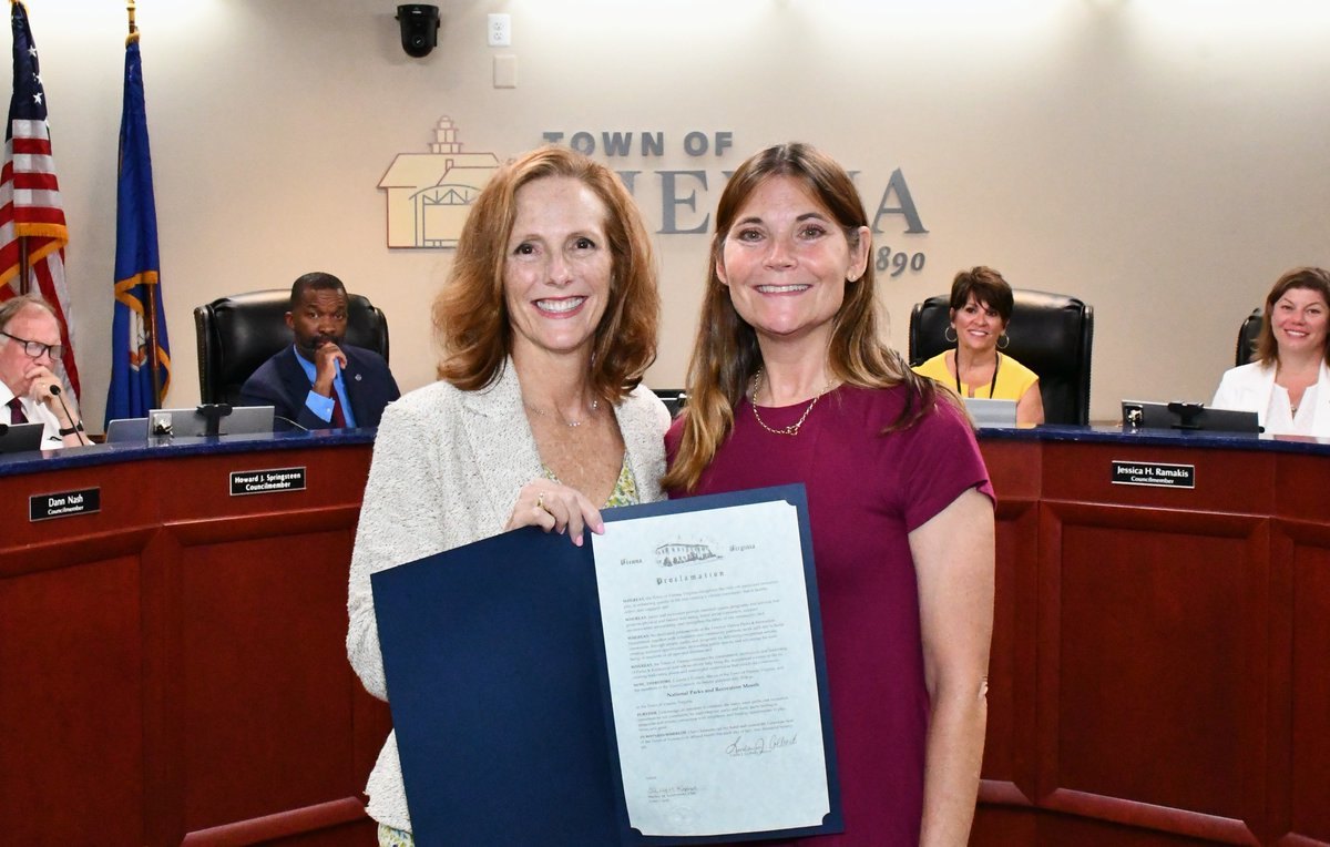 Two women hold a framed proclamation document at a Town of Vienna council meeting.