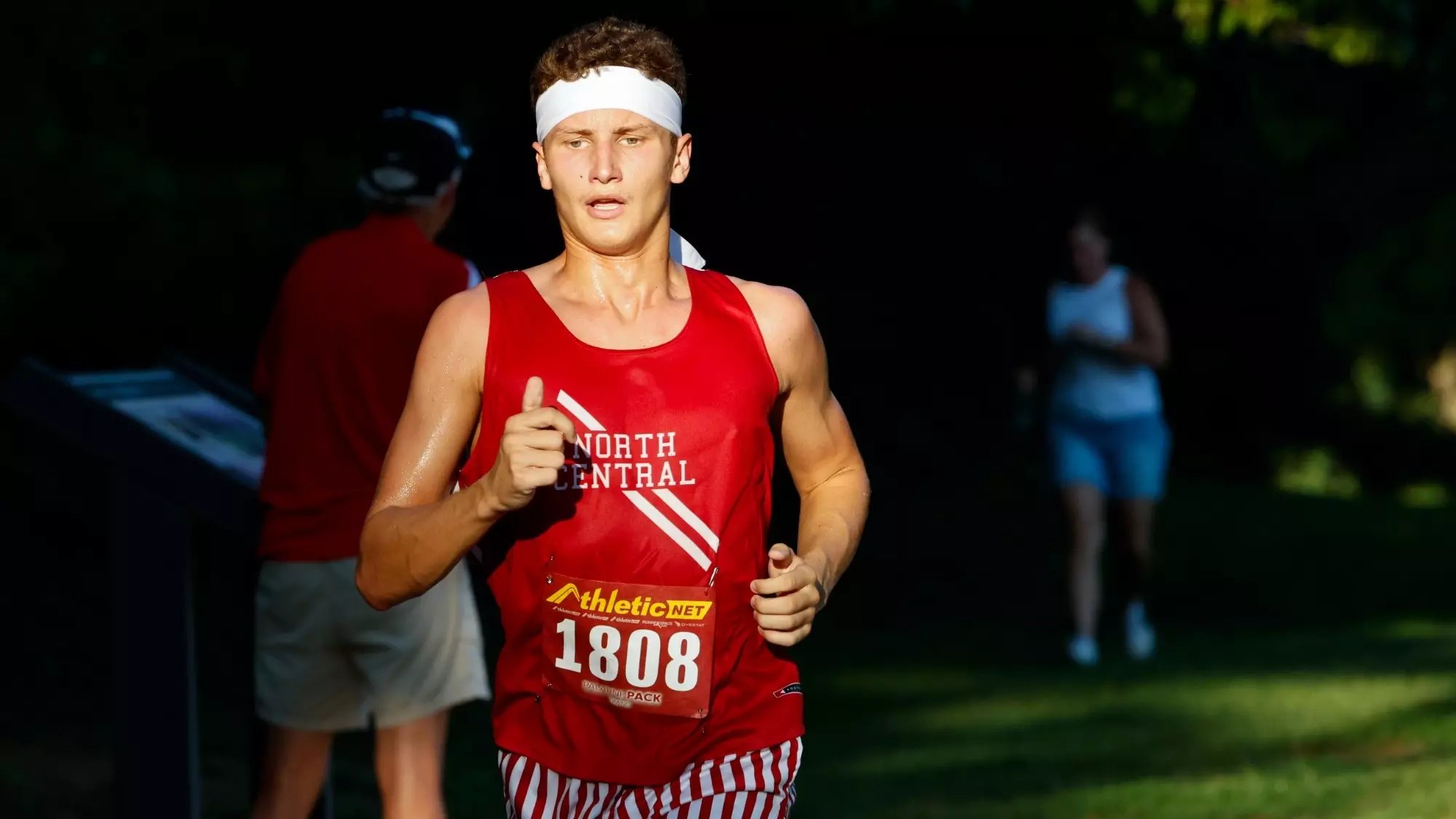 Male runner in a red North Central singlet and race bib competing outdoors.