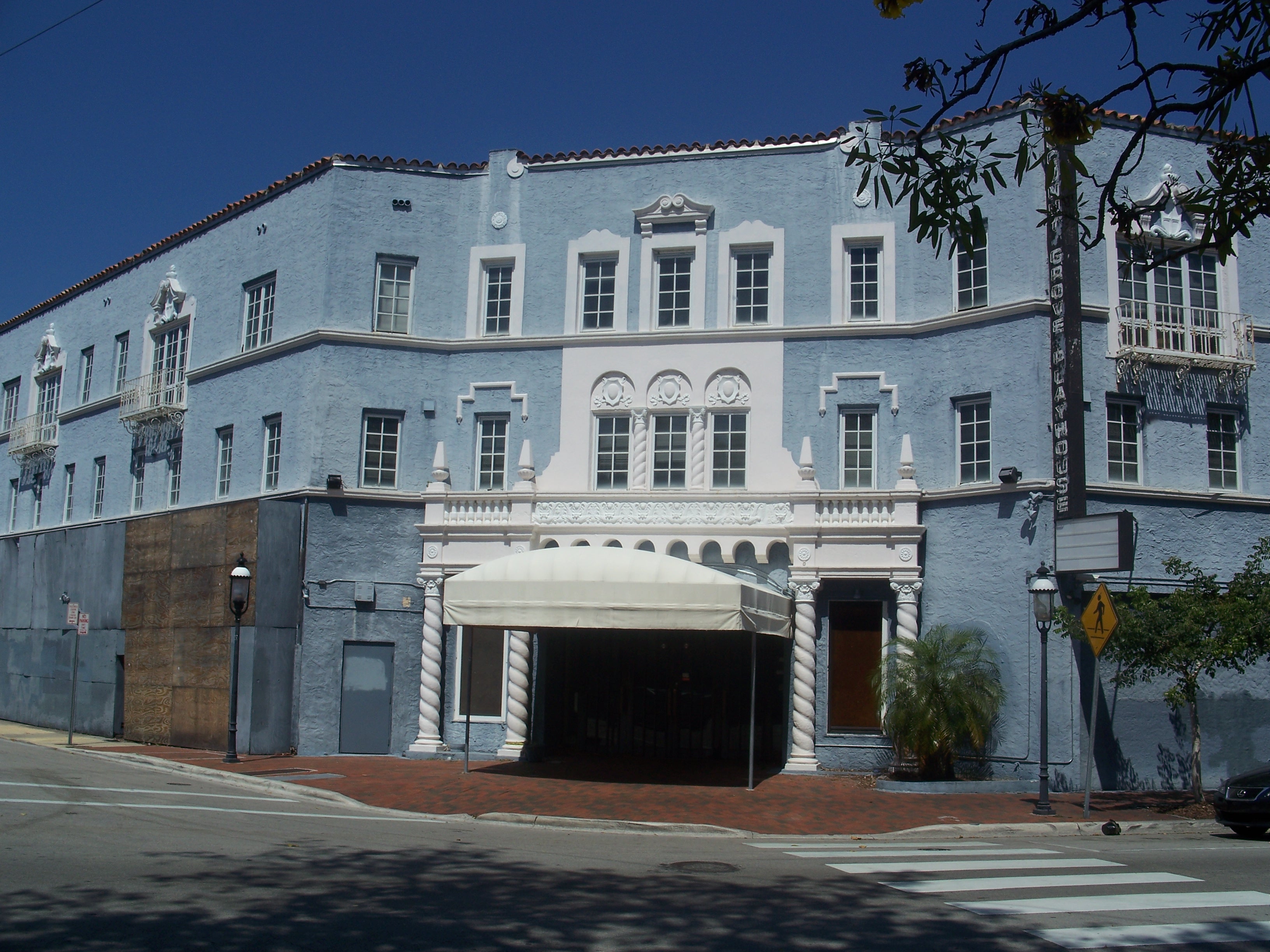 Light-blue multi-story building with white ornate trim and a canopy entrance on a street corner.