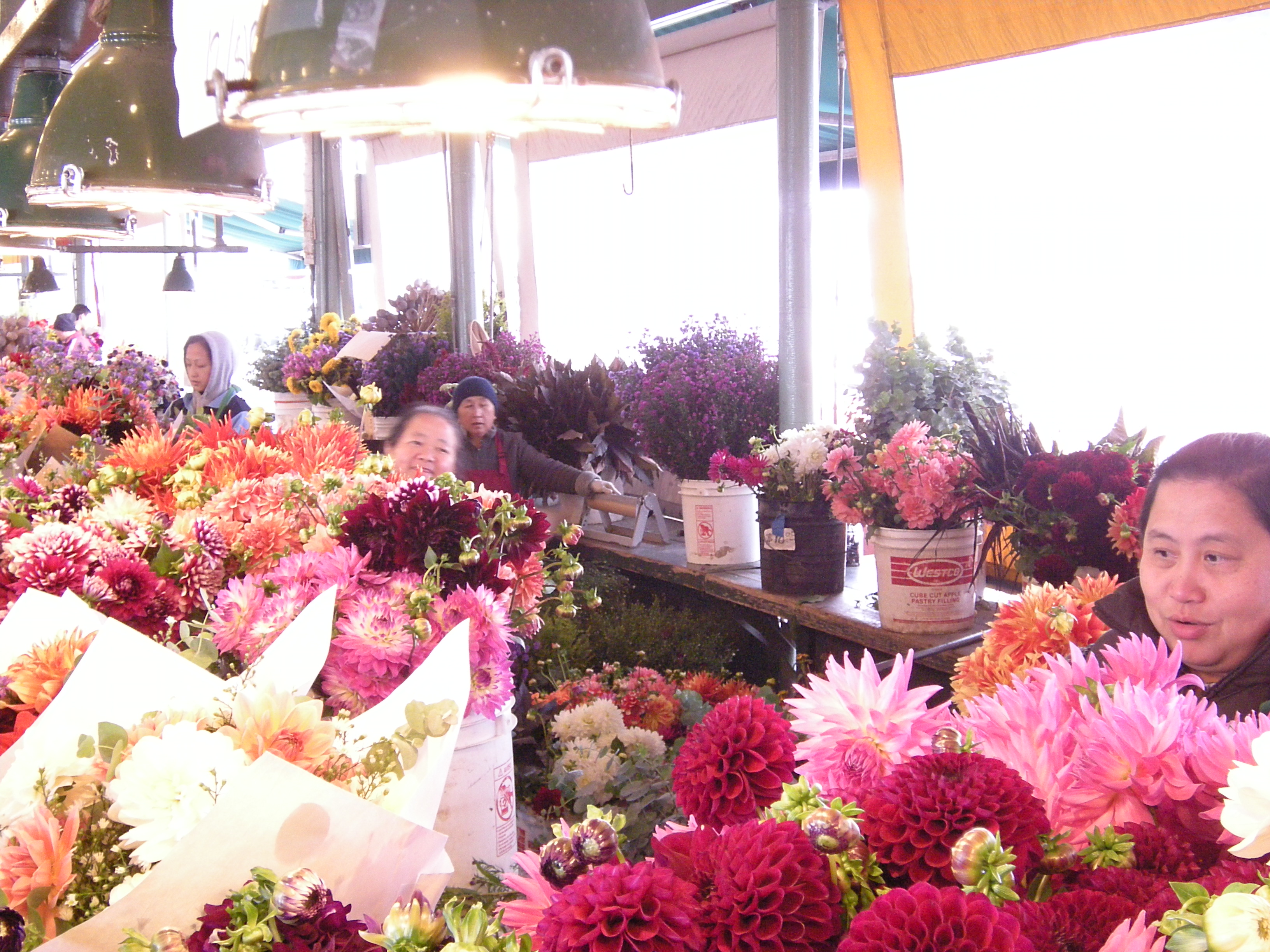 Colorful flower bouquets including dahlias fill a busy market stall under hanging lamps at Pike Place Market.