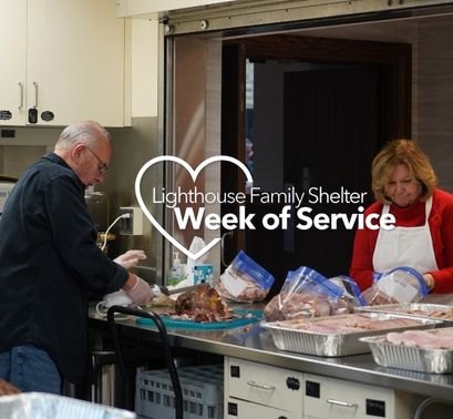 Two apron-clad volunteers package trays of food in a commercial kitchen.