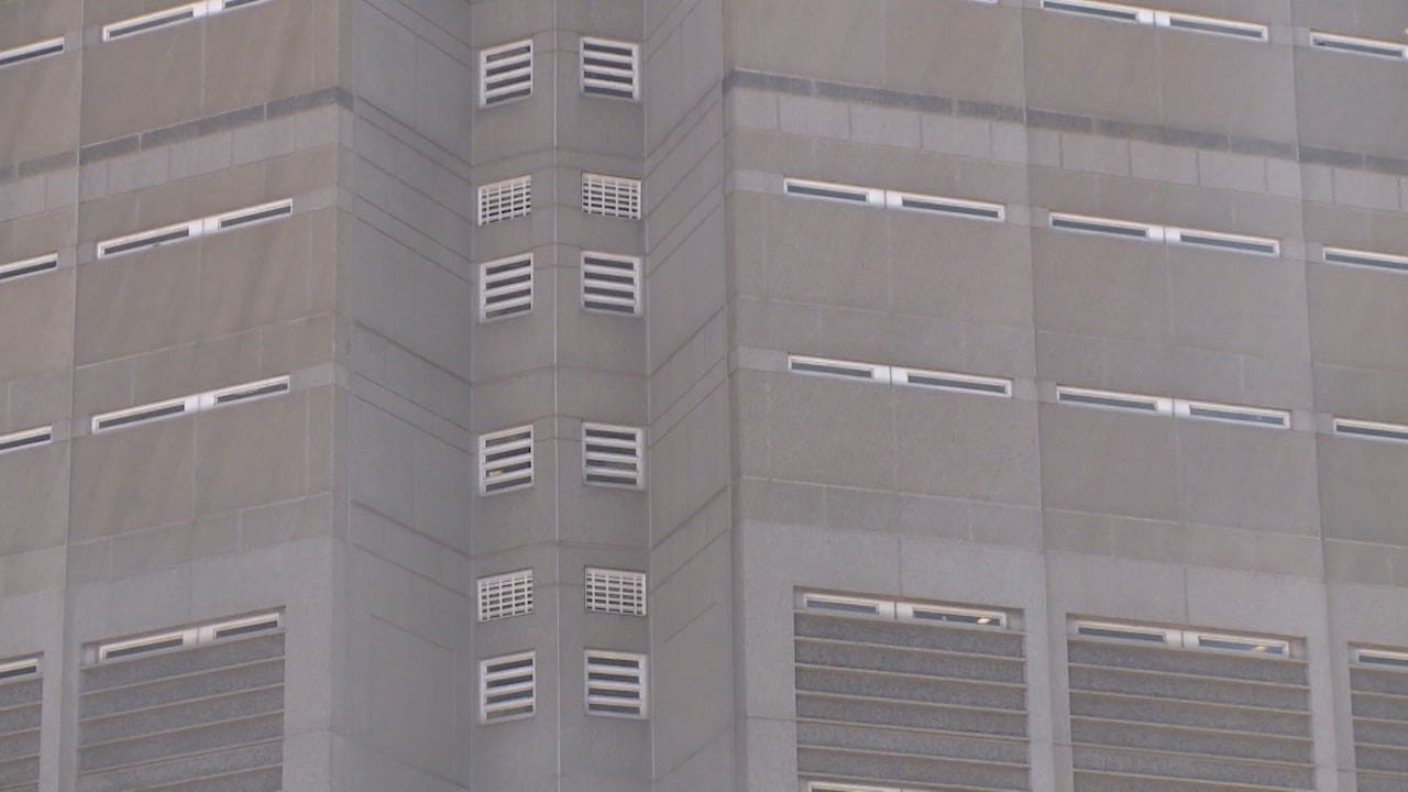 Exterior corner view of a multi-story gray concrete institutional building with louvered vents and narrow windows.
