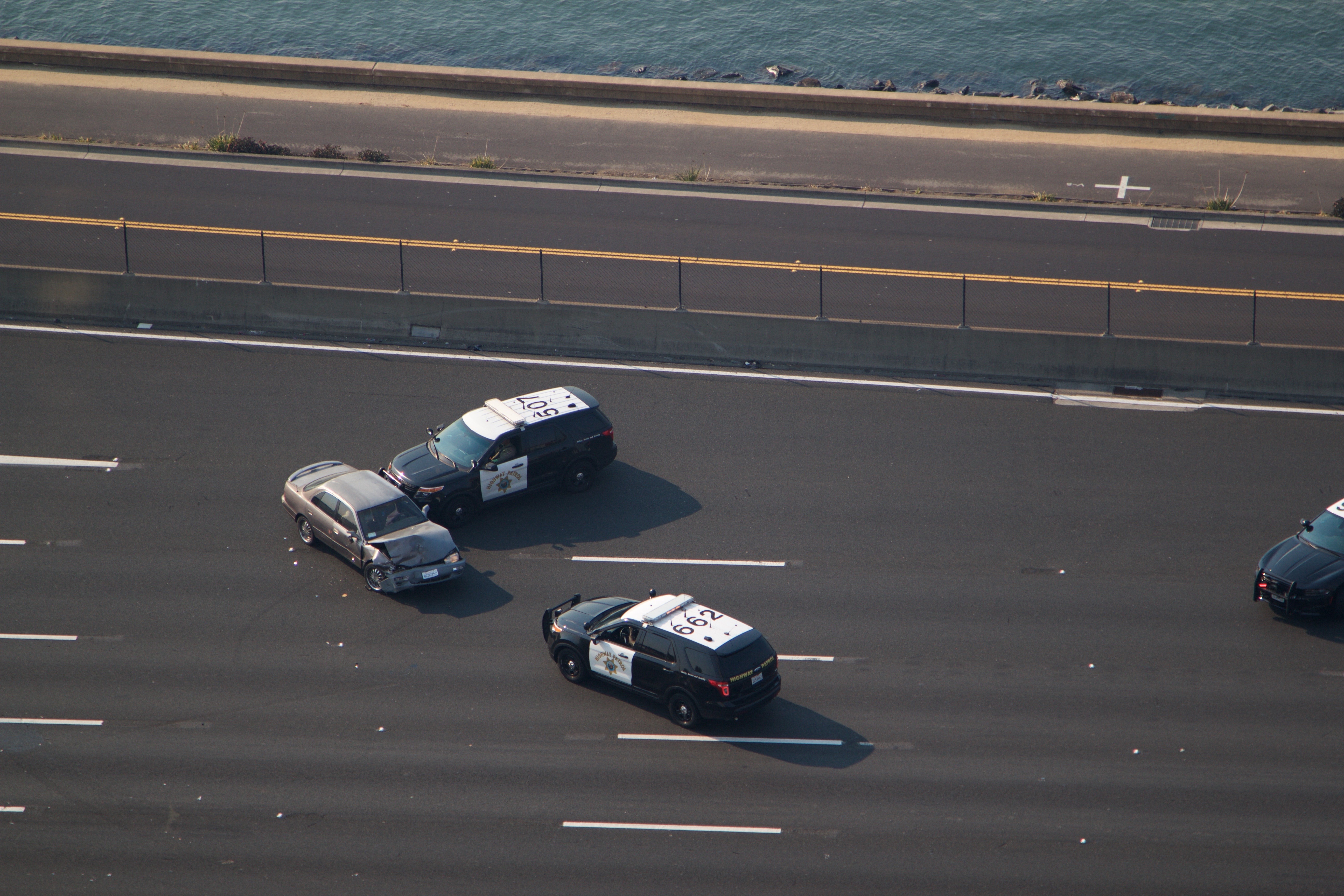 Two black-and-white law enforcement SUVs alongside a civilian sedan on a highway, aerial view.
