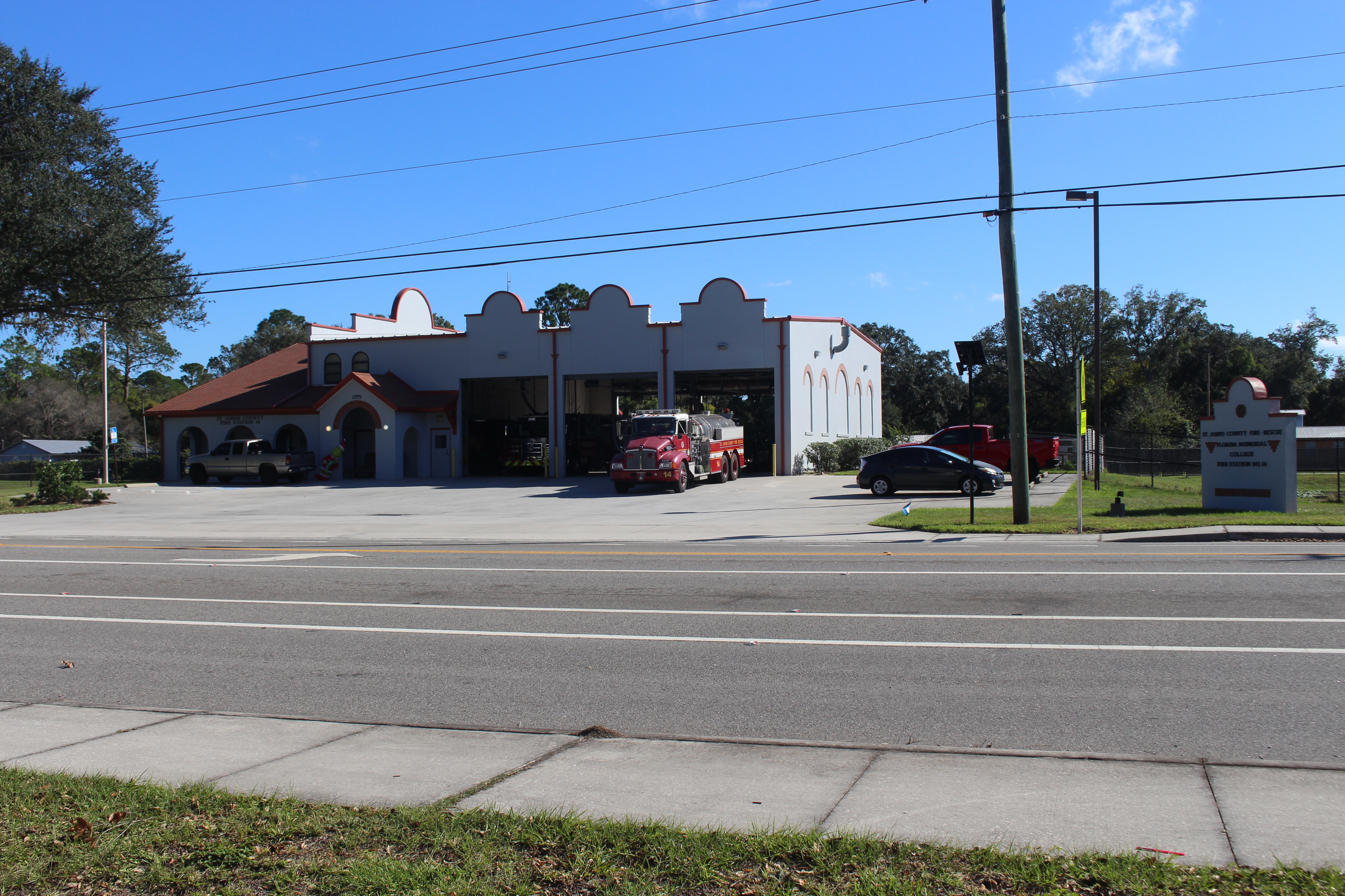 White stucco fire station with multiple bay doors and a red fire engine inside.
