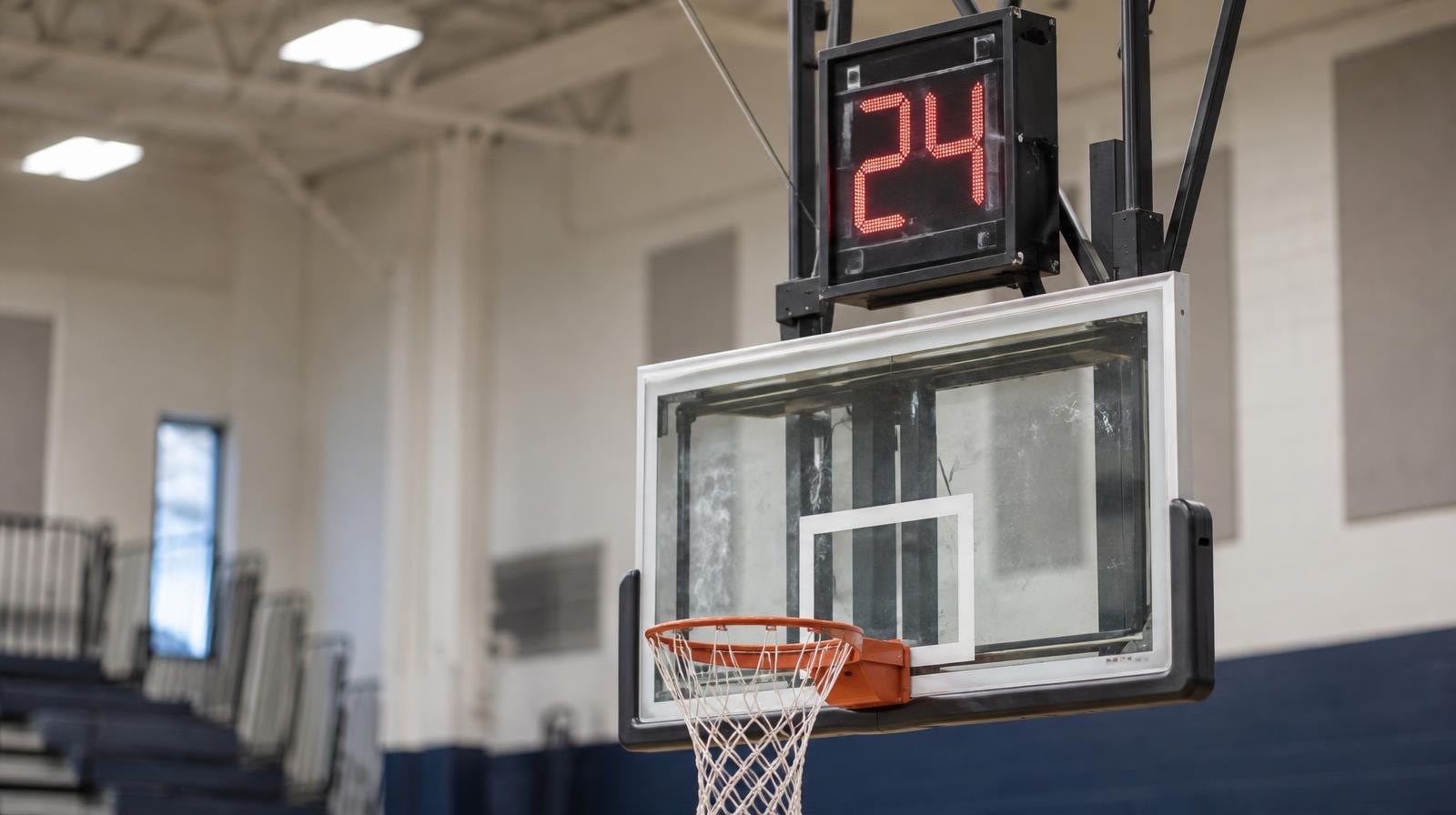 A shot clock display mounted above a basketball backboard in a brightly lit gymnasium.