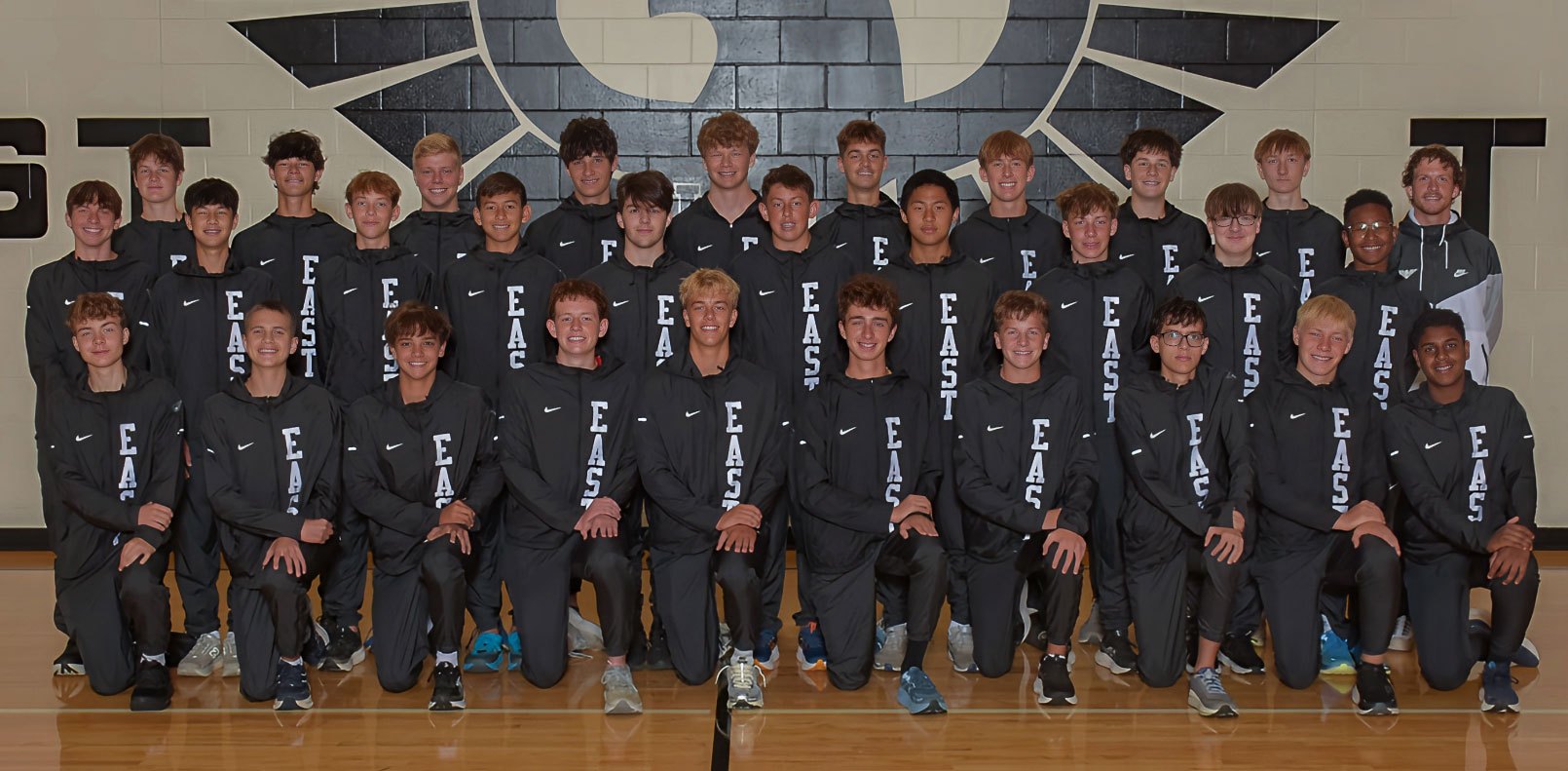 Group of male athletes in matching dark 'EAST' Nike tops posed in rows in a gymnasium.