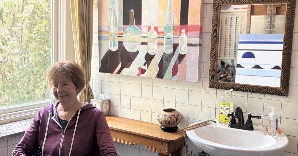 A woman in a purple hoodie sits in a tiled room with colorful abstract paintings on the wall.