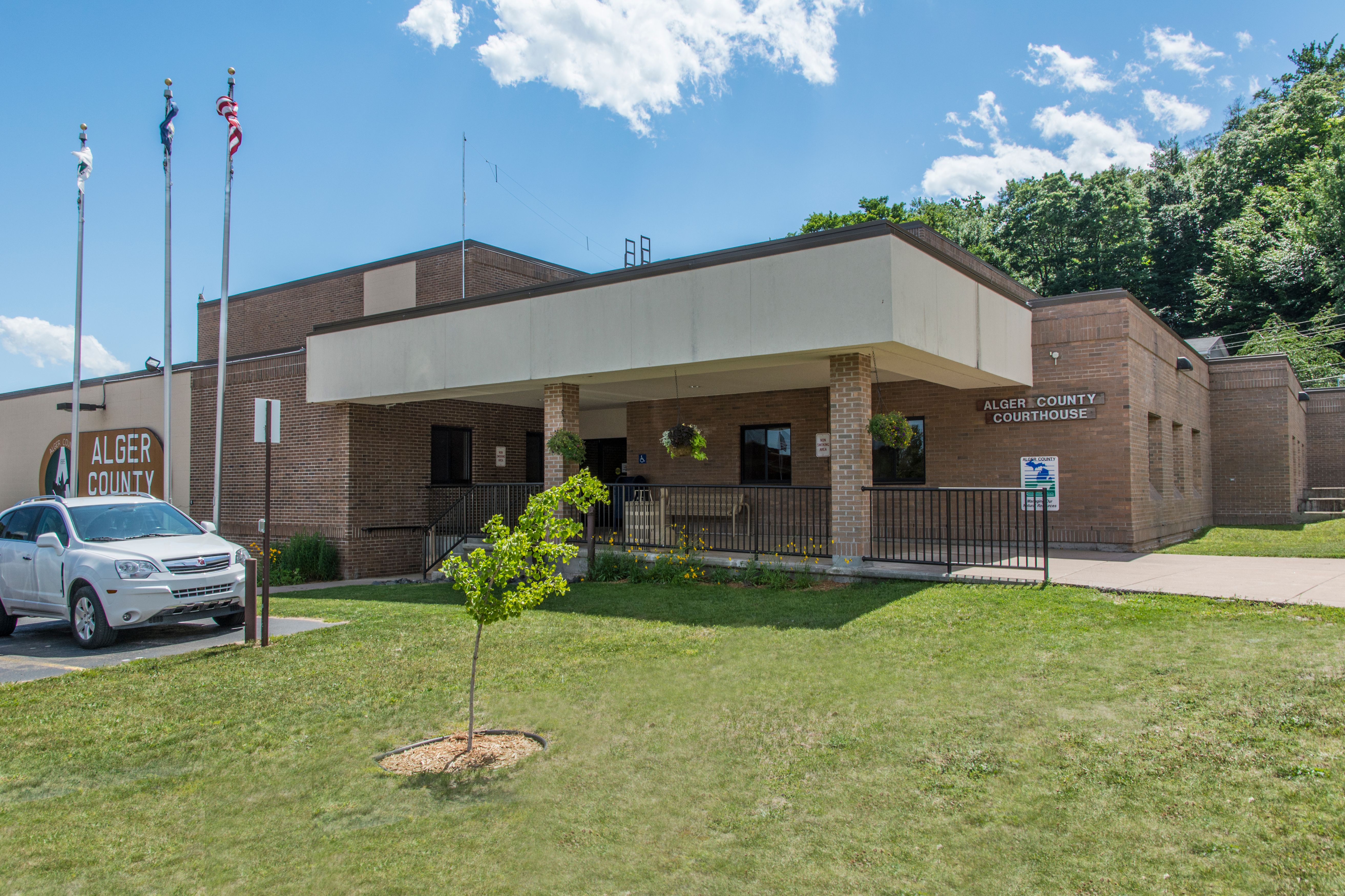 Single-story brick government building with flagpoles on a grassy lawn.