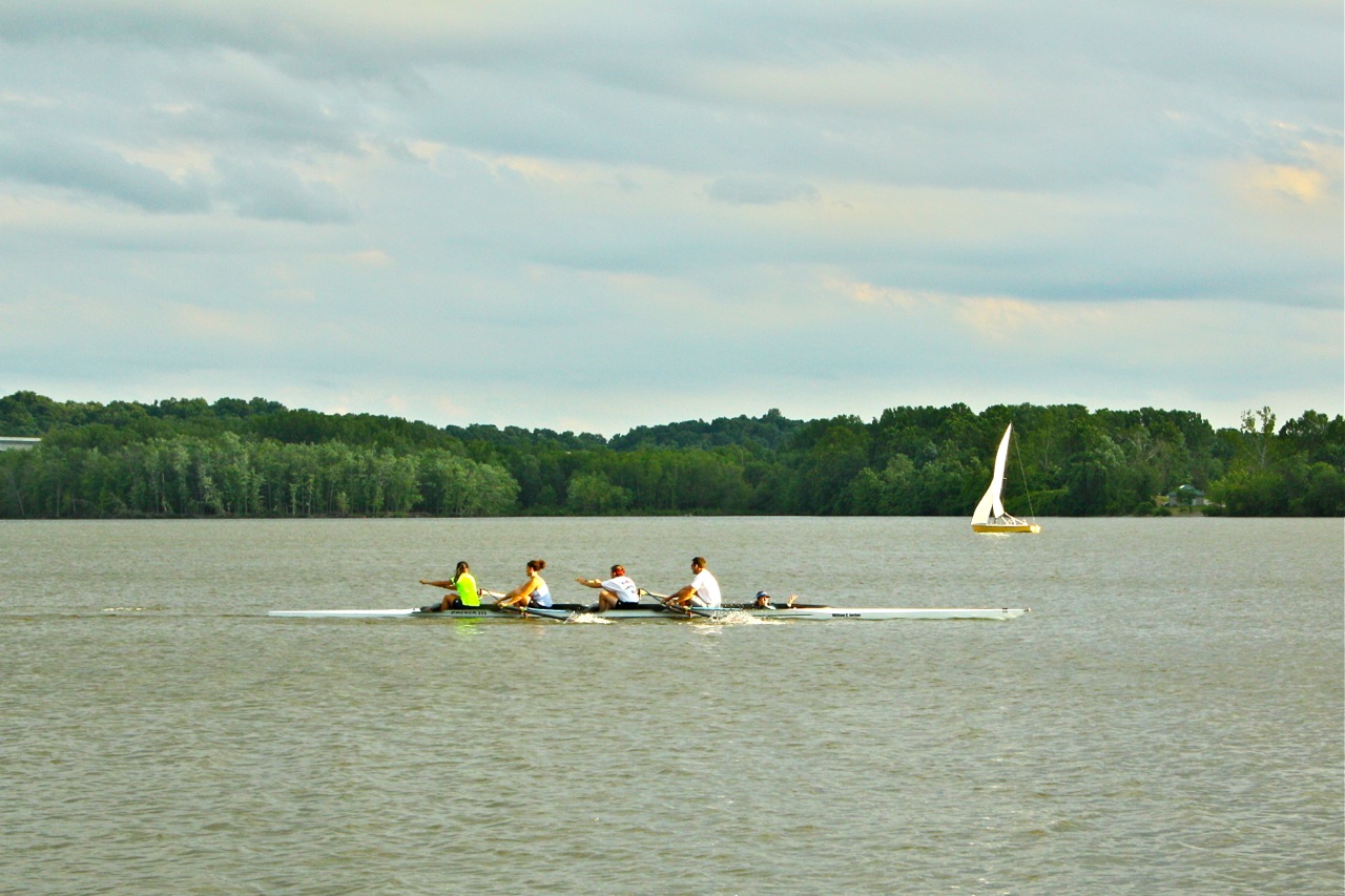 Four rowers in a narrow racing shell on a calm, wide lake.