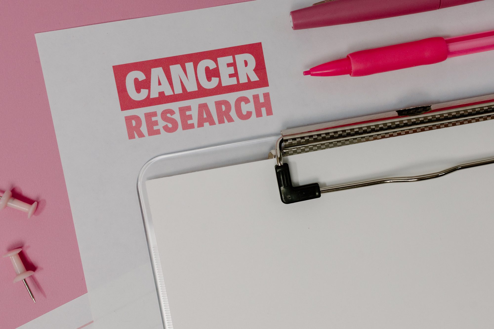 Flat lay of a cancer research paper on a clipboard with pink stationery items.