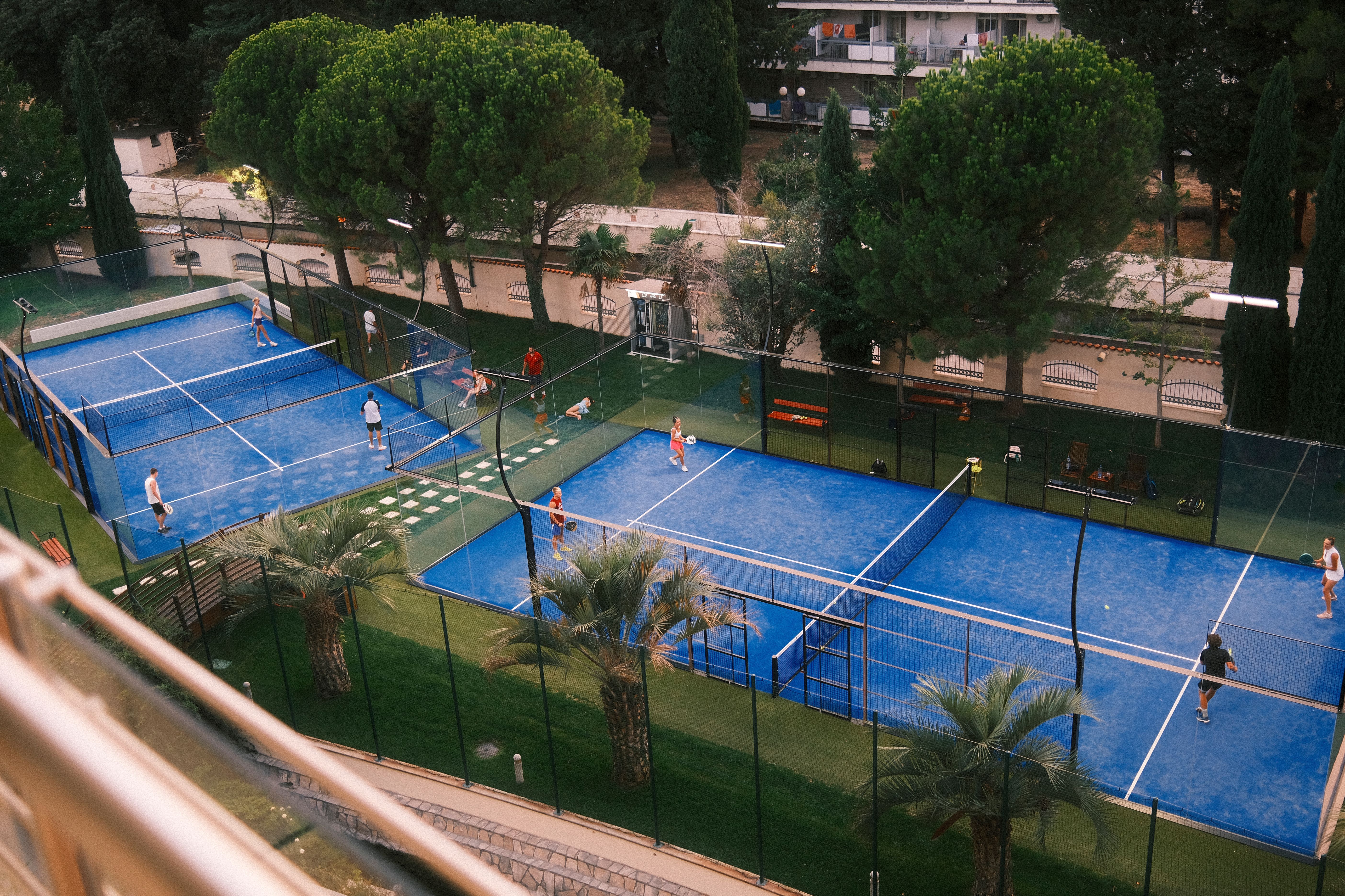 Aerial view of players competing on multiple blue outdoor tennis courts.
