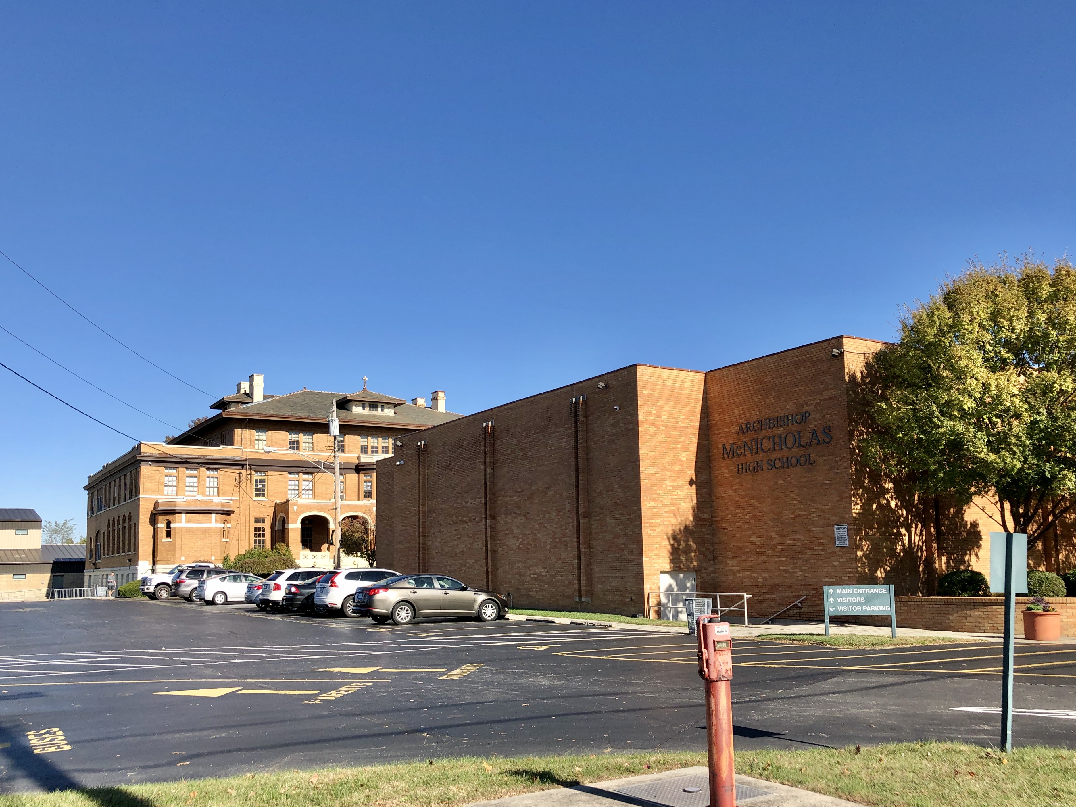 Multi-story brick school building with parking lot and autumn foliage.