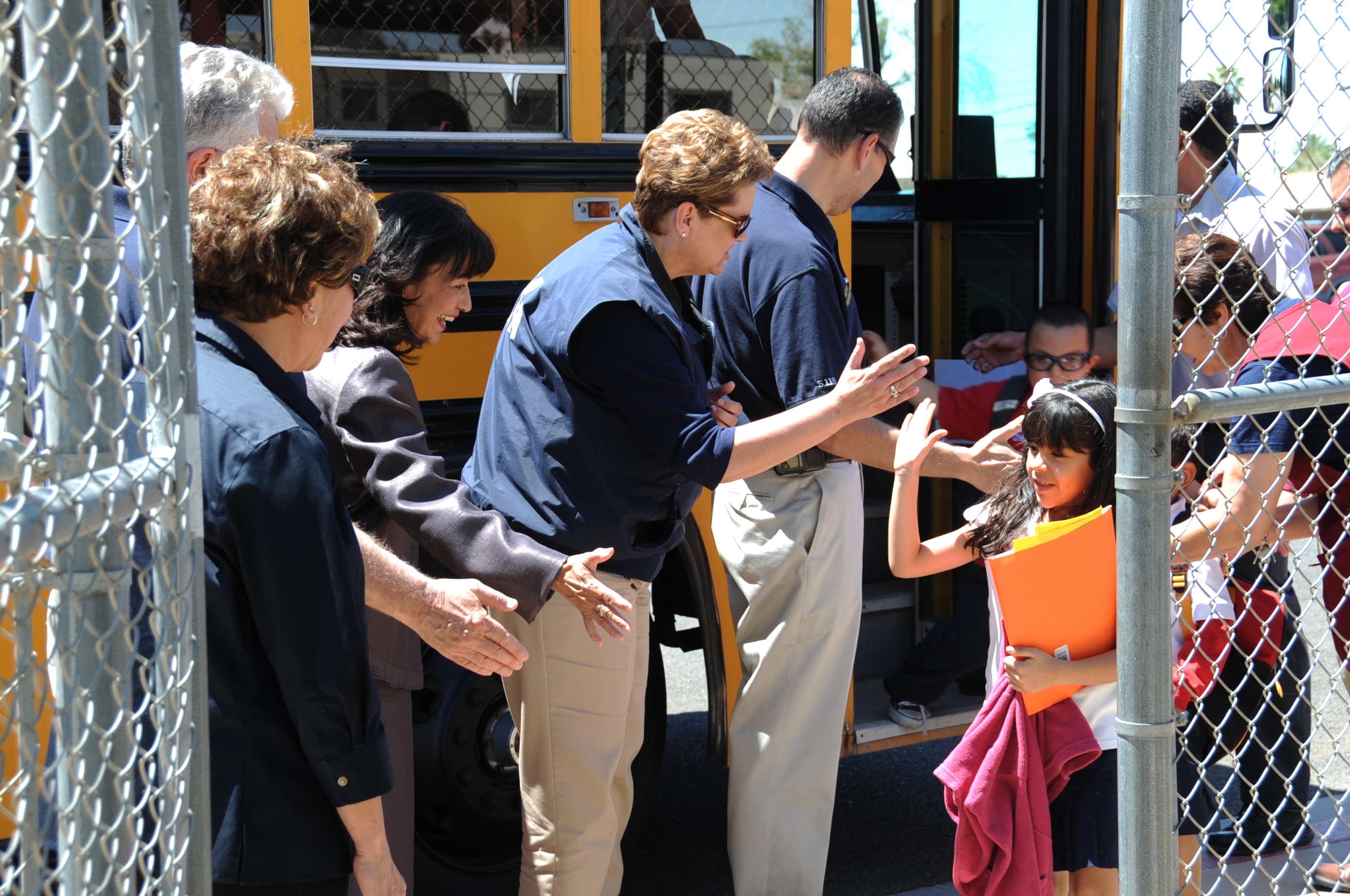 Adults high-fiving young children as they exit a yellow school bus outdoors.