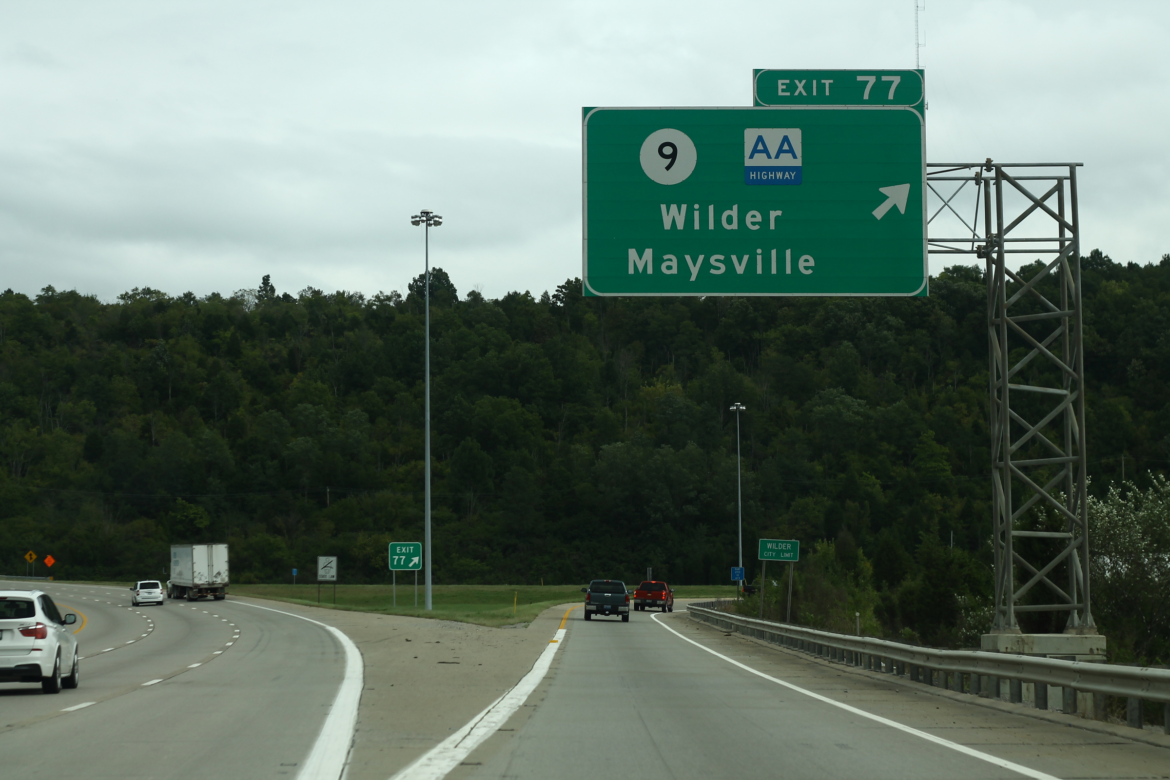 Green overhead exit sign on a multi-lane interstate highway with light traffic.