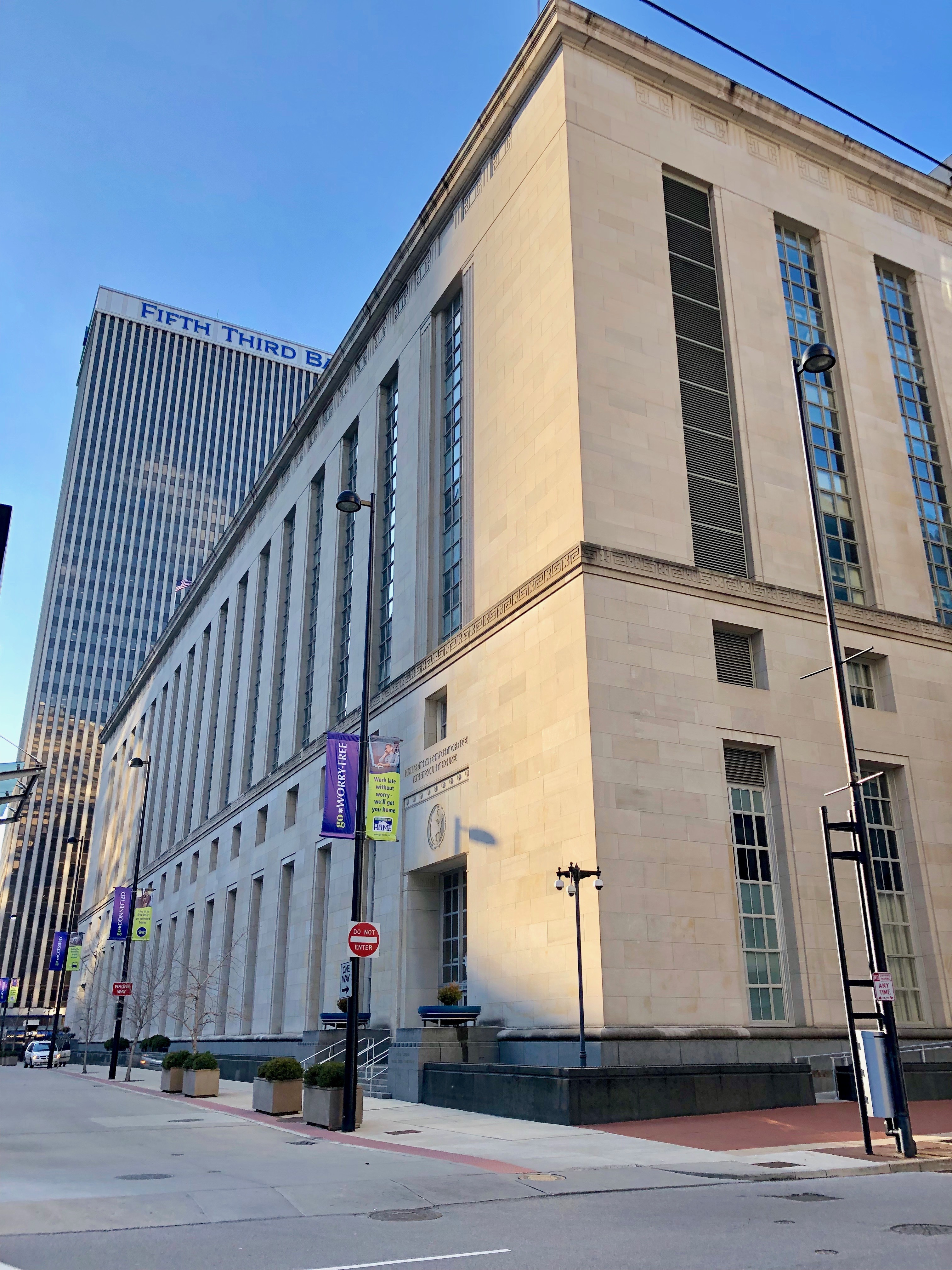 Neoclassical stone federal courthouse on a downtown Cincinnati street corner under a blue sky.
