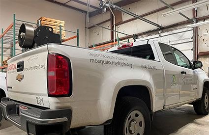 White pickup truck with public health mosquito program branding and a large sprayer in the truck bed.