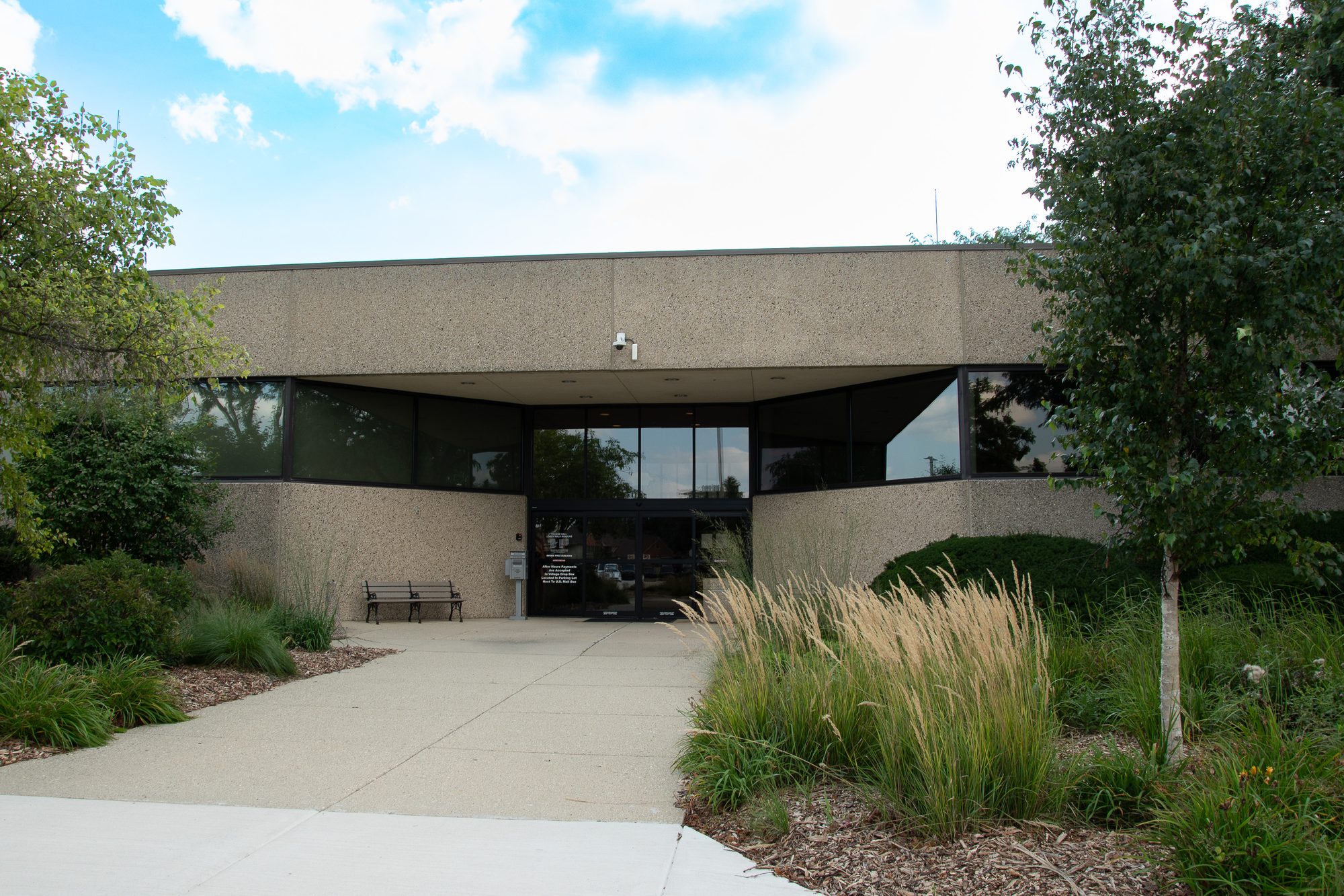 Low-rise tan municipal building with dark glass panels and a landscaped entrance walkway.