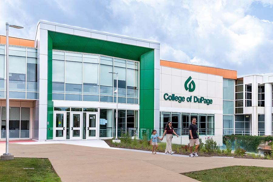 Exterior of a college building with green accents, the institution's logo, and people walking on the plaza.