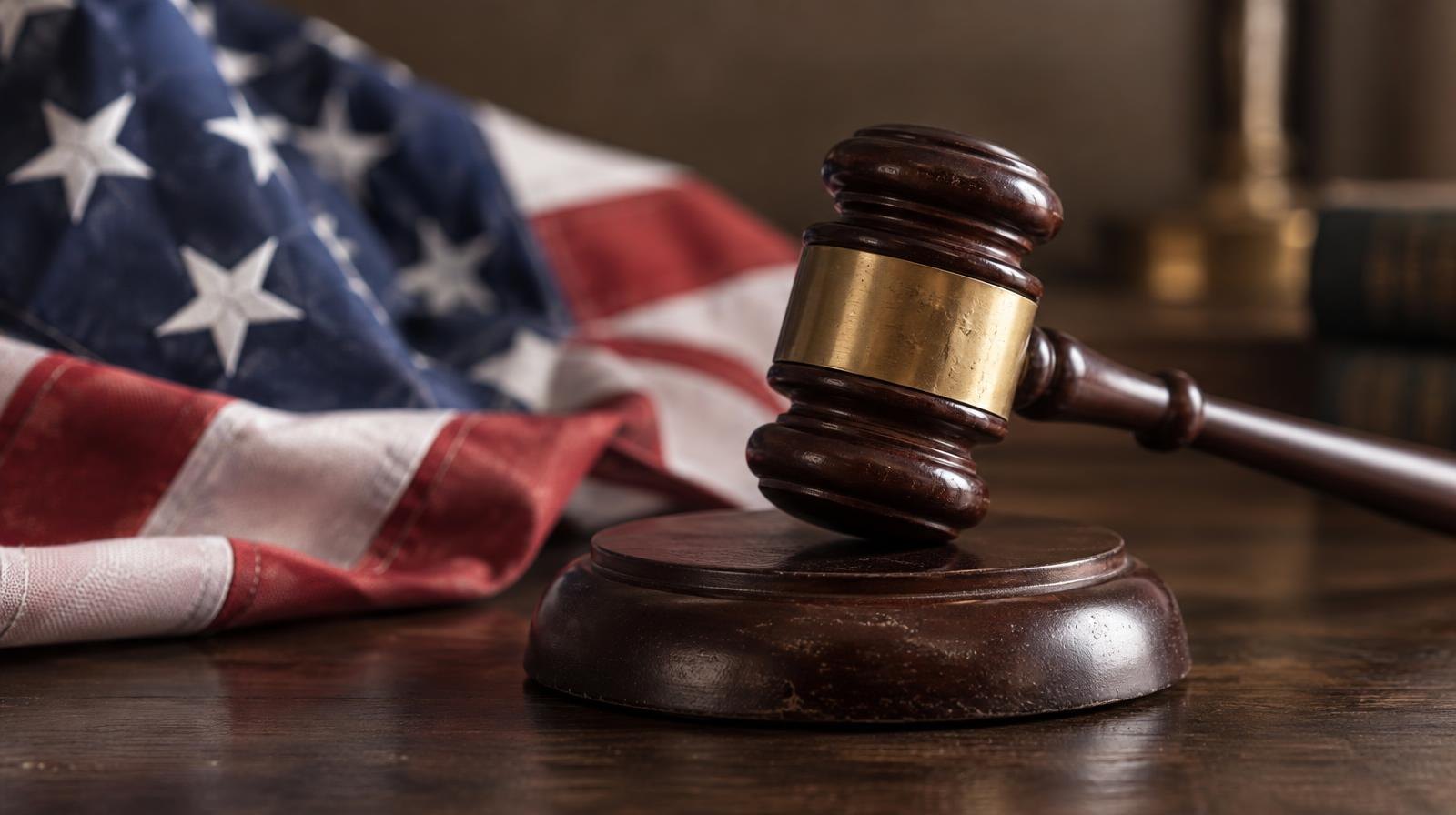 A wooden gavel resting on its sound block beside a folded American flag.