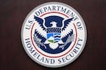 U.S. Department of Homeland Security seal mounted on a dark wood-paneled wall.