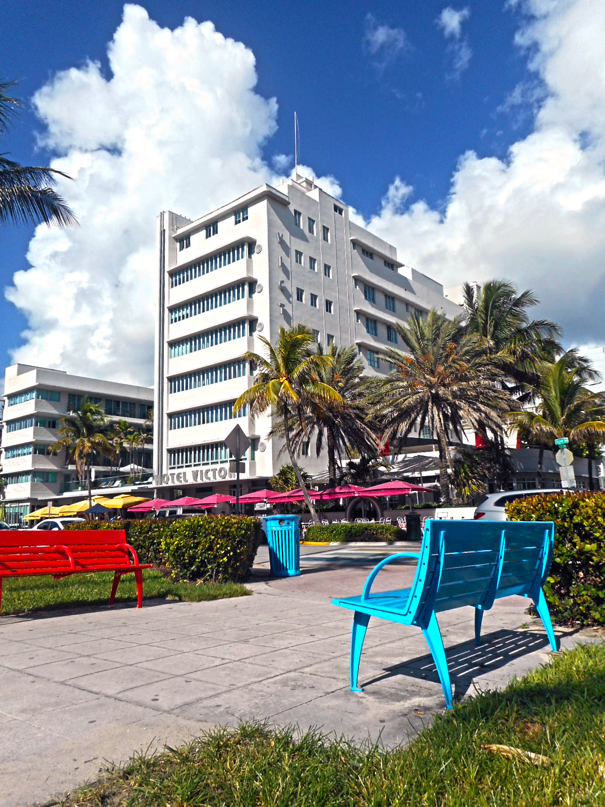 Colorful red and blue park benches with palm trees and a white Art Deco hotel in the background.