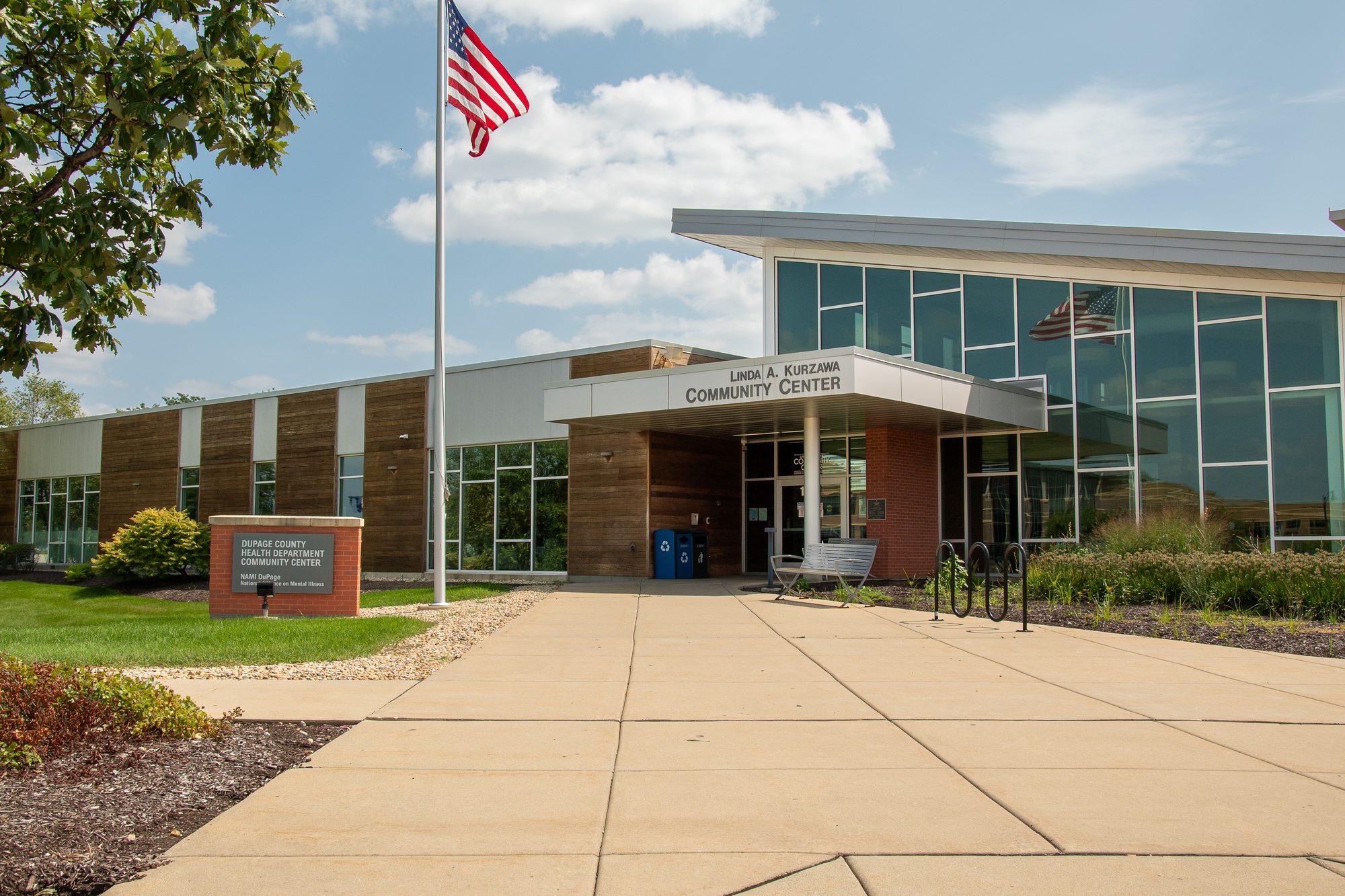 Exterior of a modern single-story community center building with glass facade and American flag.