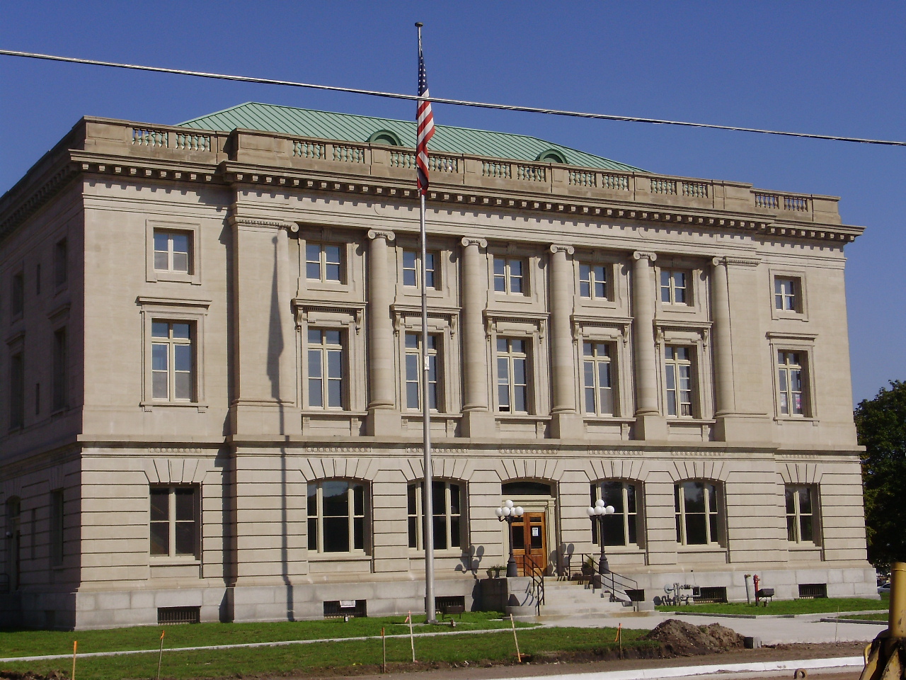 Neoclassical stone city hall building with green copper roof and American flag.