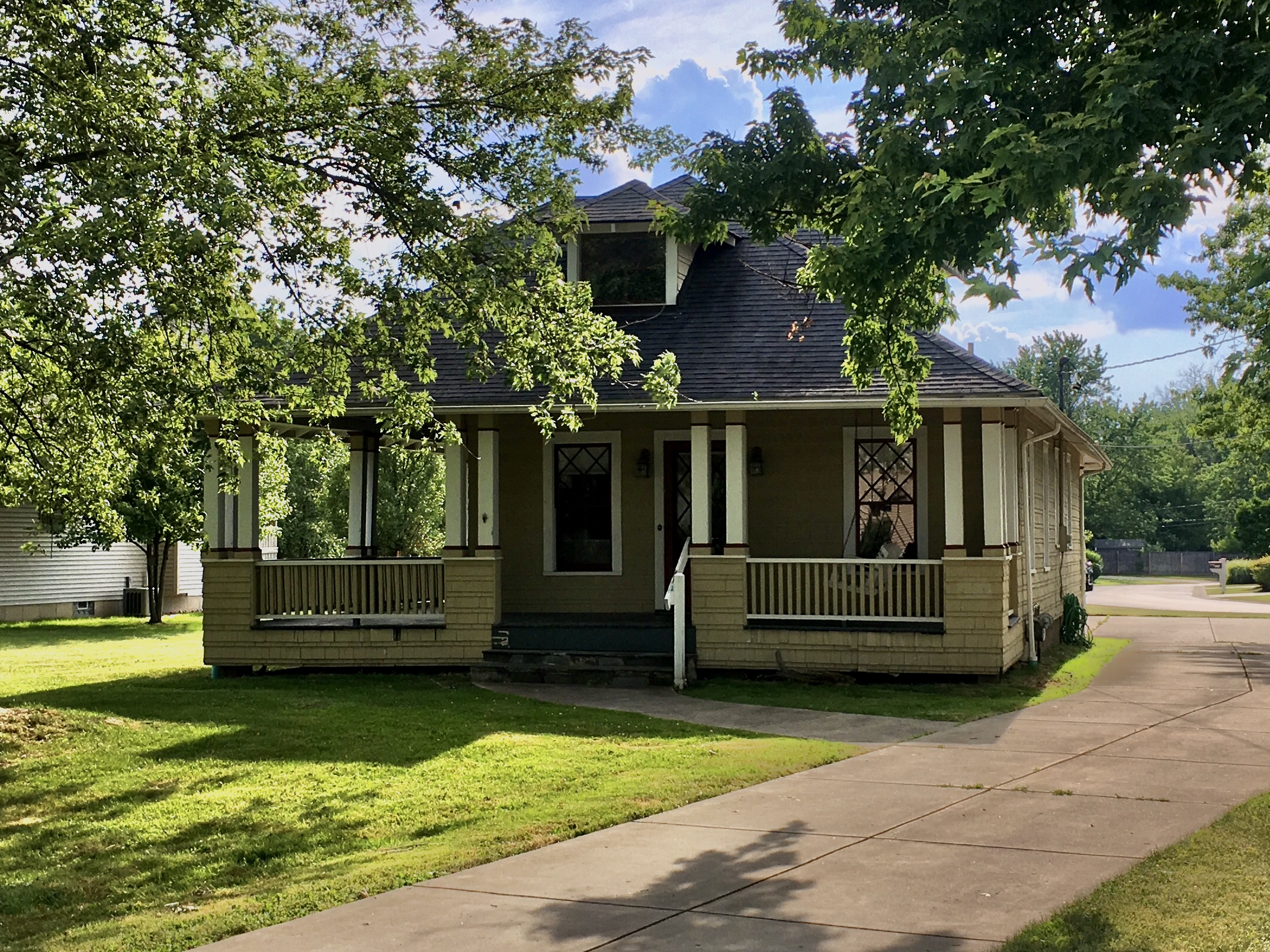 A one-and-a-half-story house with a wide hip roof and wraparound porch on a corner lot.