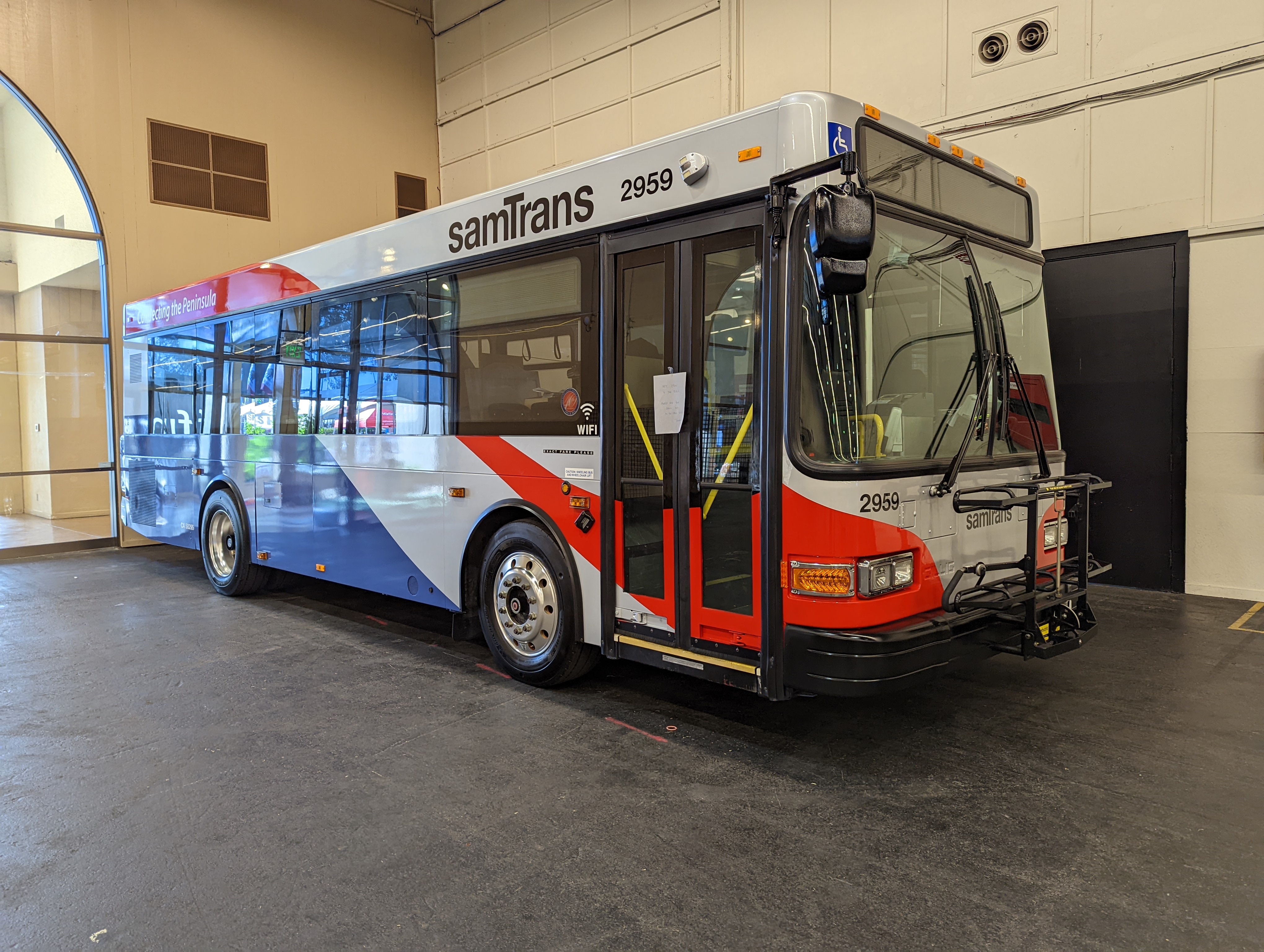 SamTrans transit bus with red, white, and blue livery parked indoors.