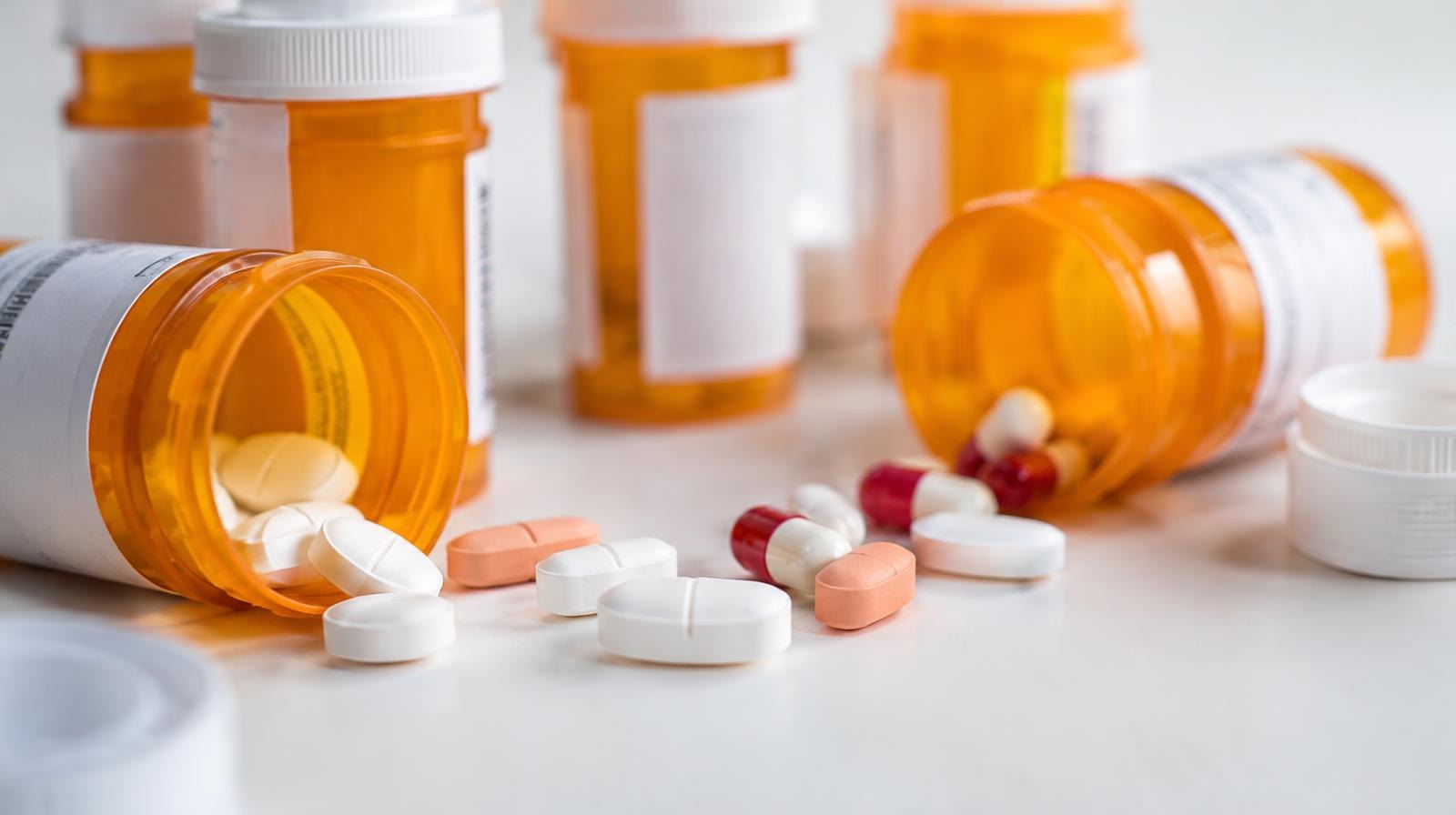 Orange prescription pill bottles with white caps and loose tablets on a white surface.