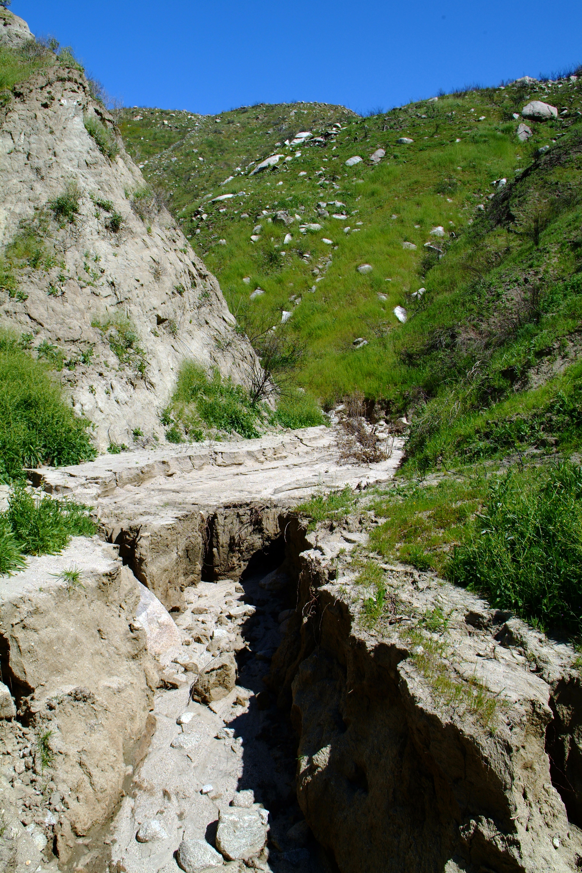 Deeply eroded dirt road with exposed rock channels cut by floodwaters.