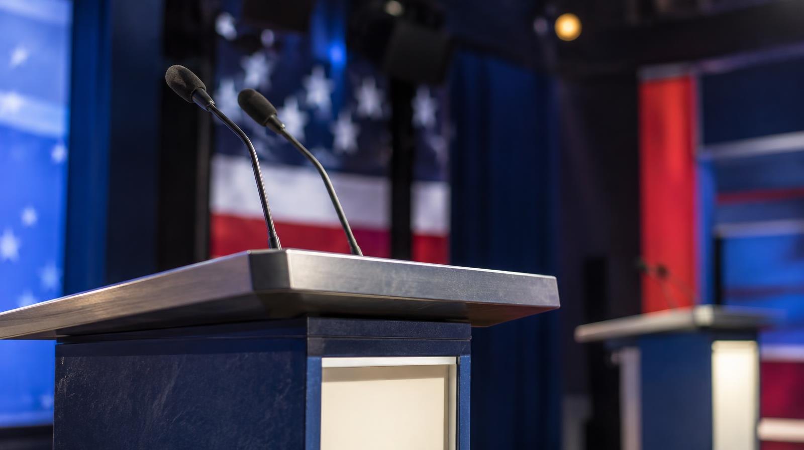 Two podiums with microphones on a lit television studio stage.