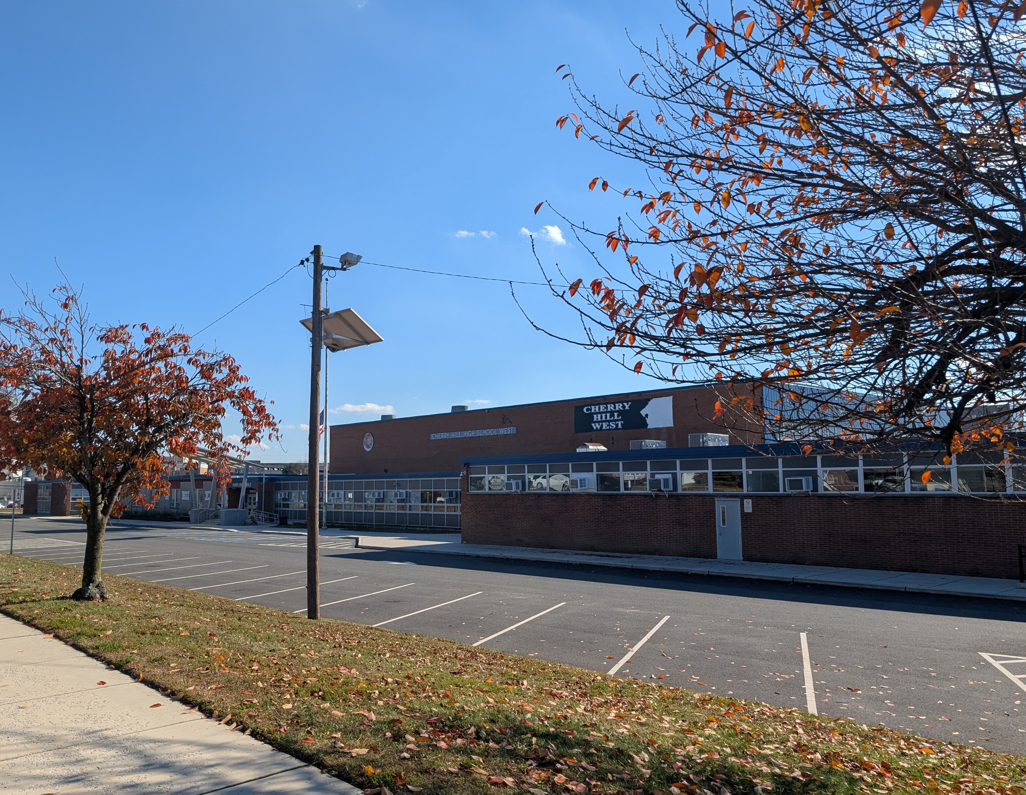 Brick exterior of a high school building with a parking lot and autumn trees in the foreground.