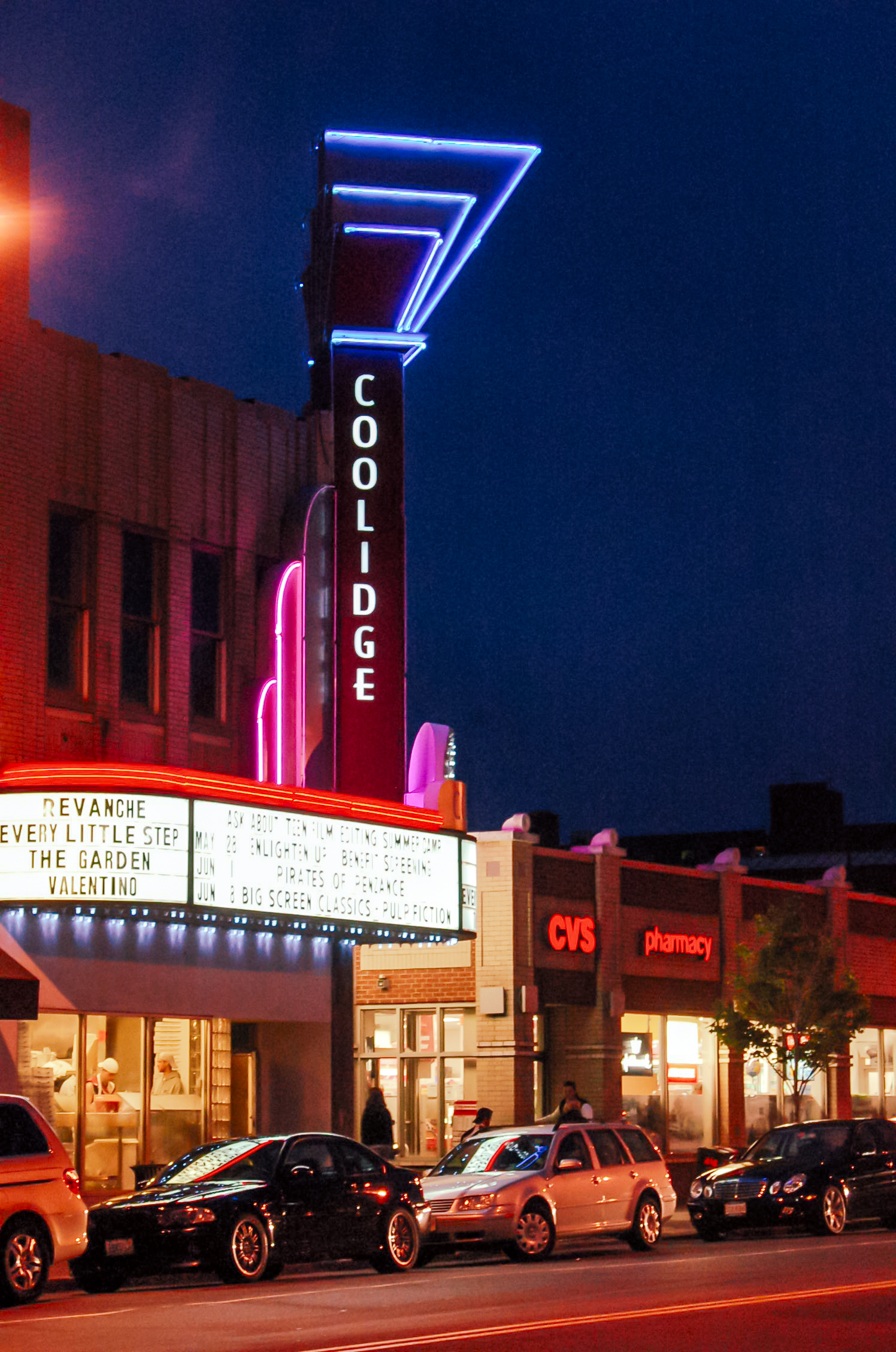 Neon-lit theater marquee glowing at night along a commercial street.