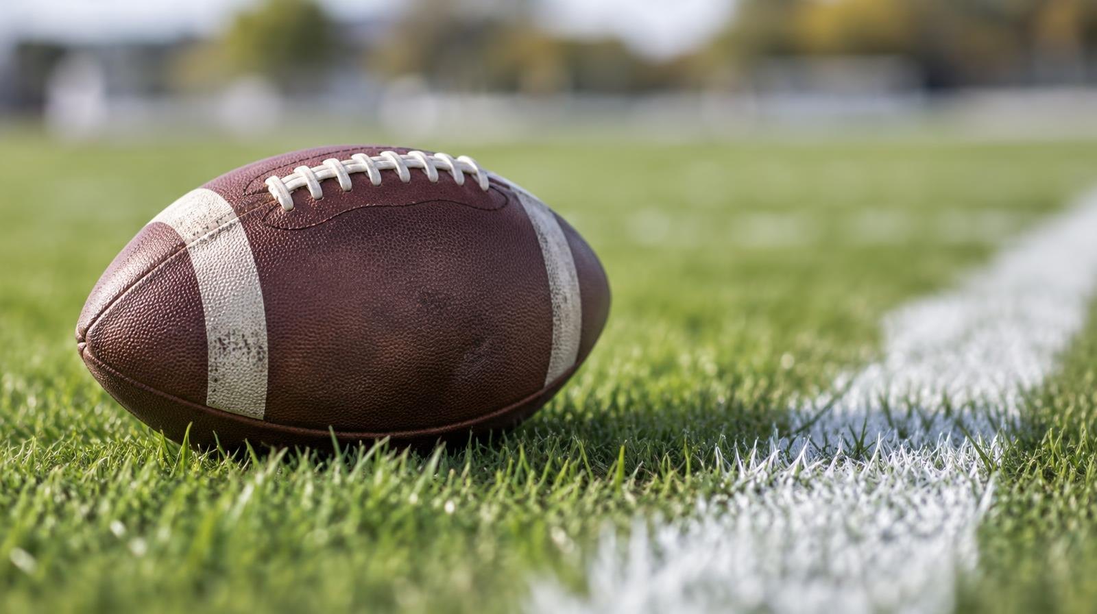 An American football resting on green grass beside a white painted yard line.
