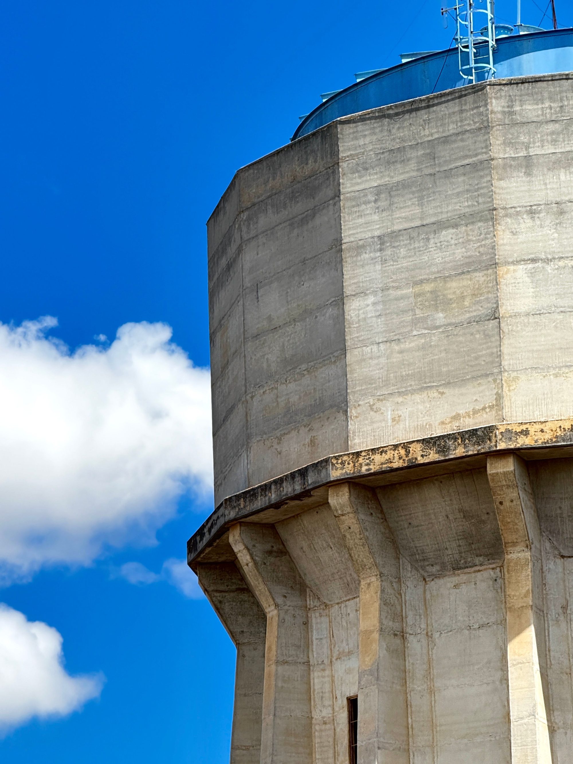 Partial view of a concrete water tower set against a clear blue sky with clouds.