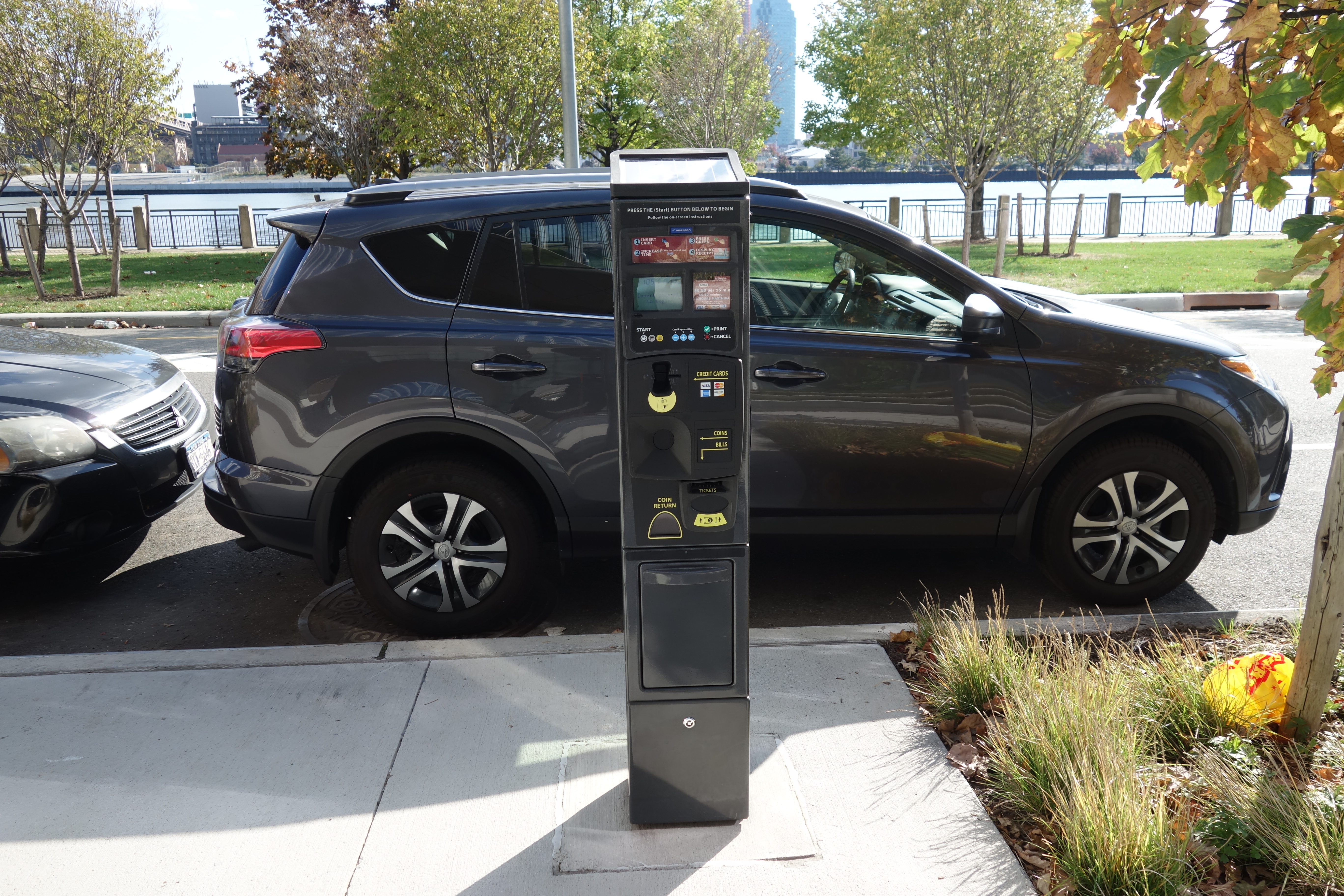 A multi-space parking pay station kiosk mounted on a sidewalk next to a parked SUV.