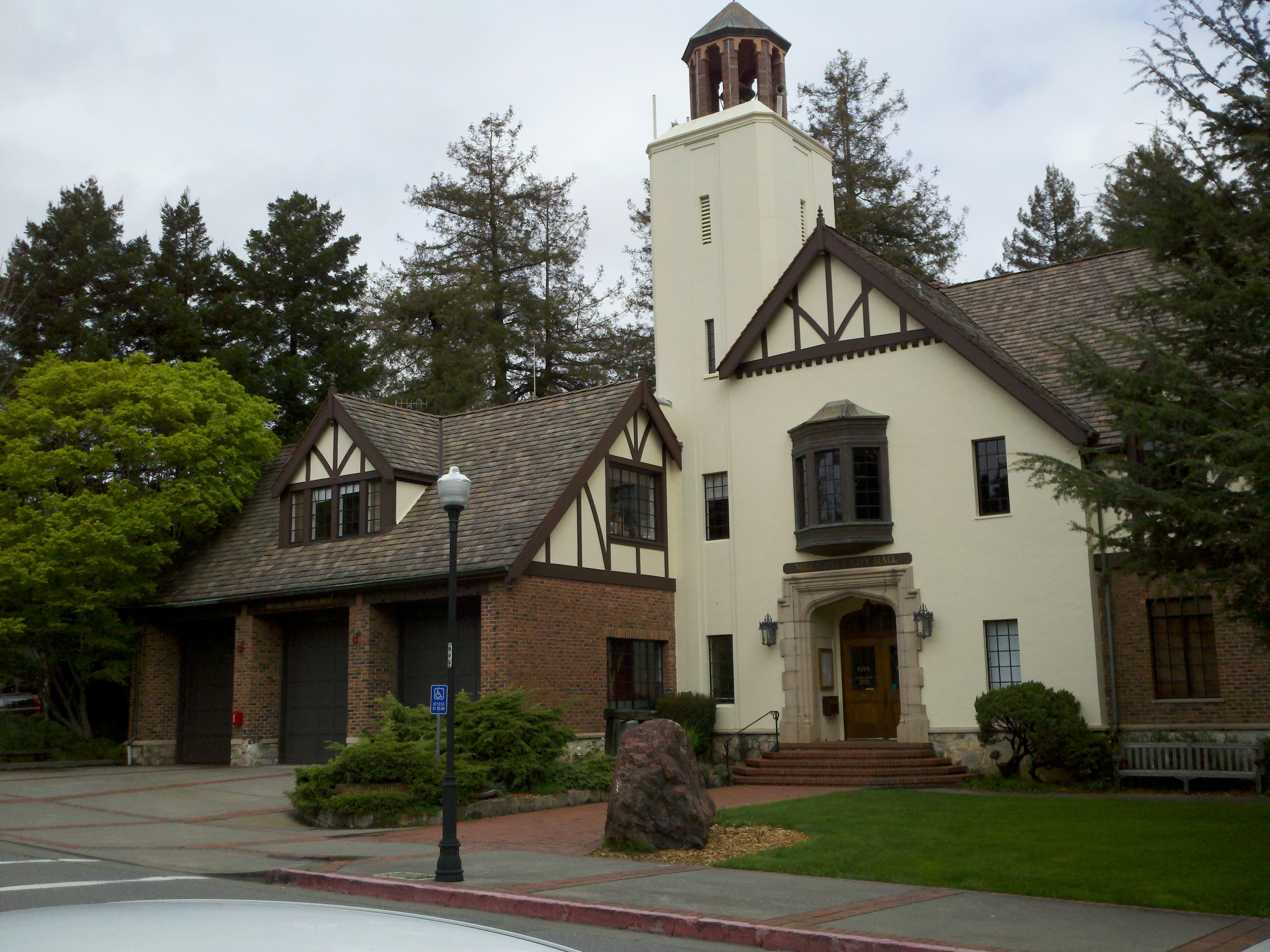 Tudor-style brick and stucco city hall building with a central tower and landscaped entrance.